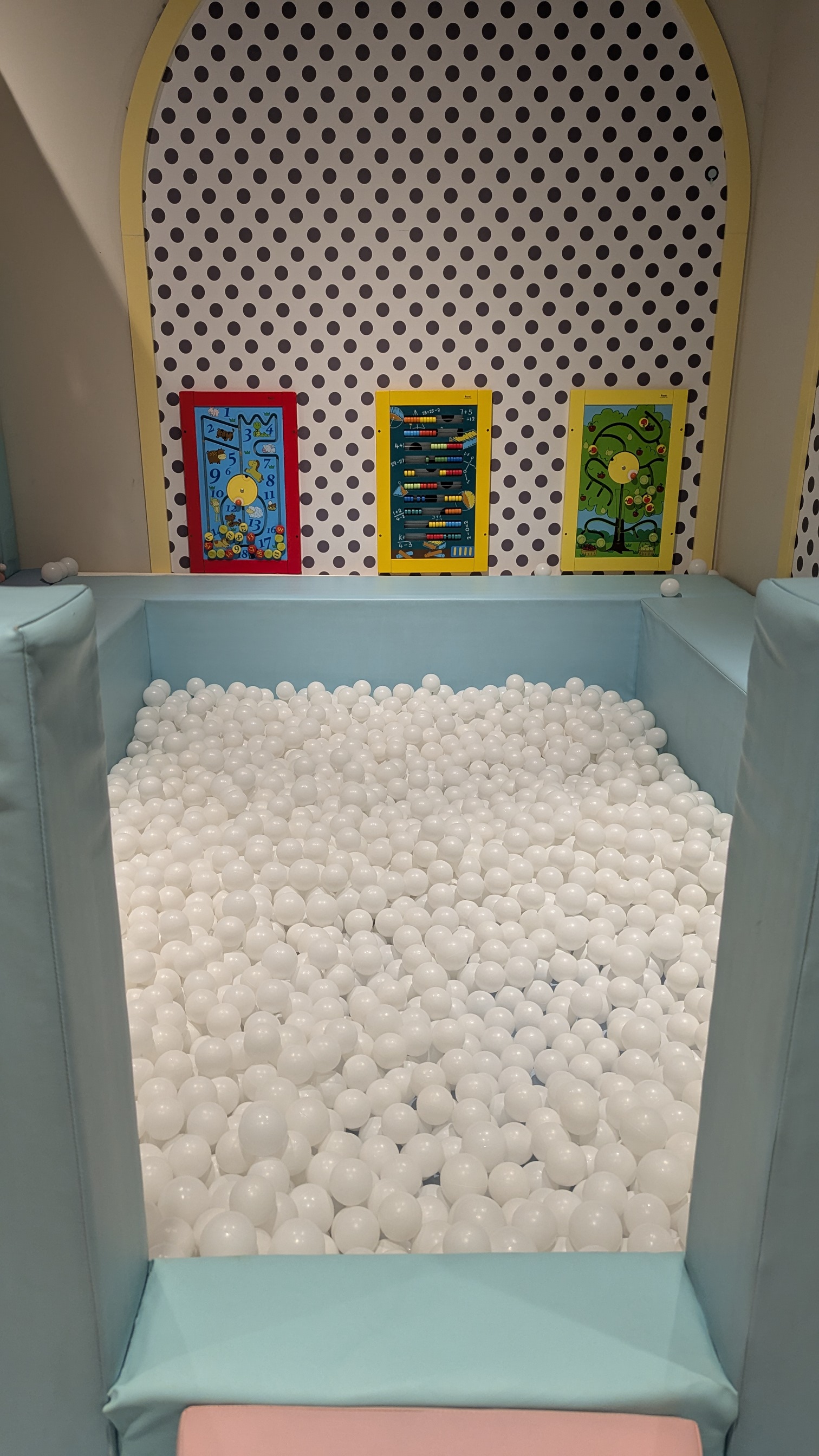 A small ball pit with interactive sliding toys in the wall.