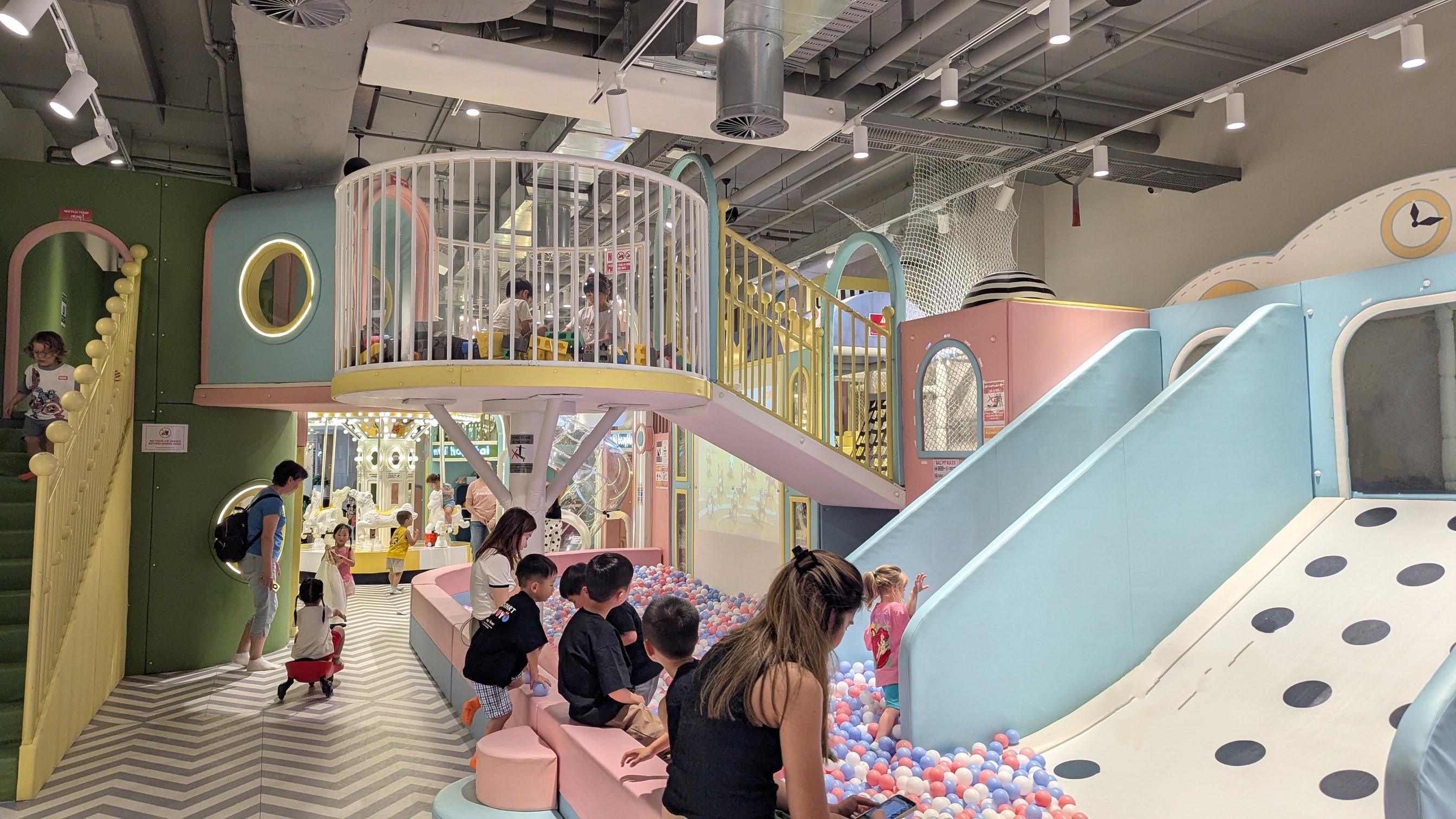 Pastel coloured indoor playground for young children featuring a slide, ball pit and small carousel.