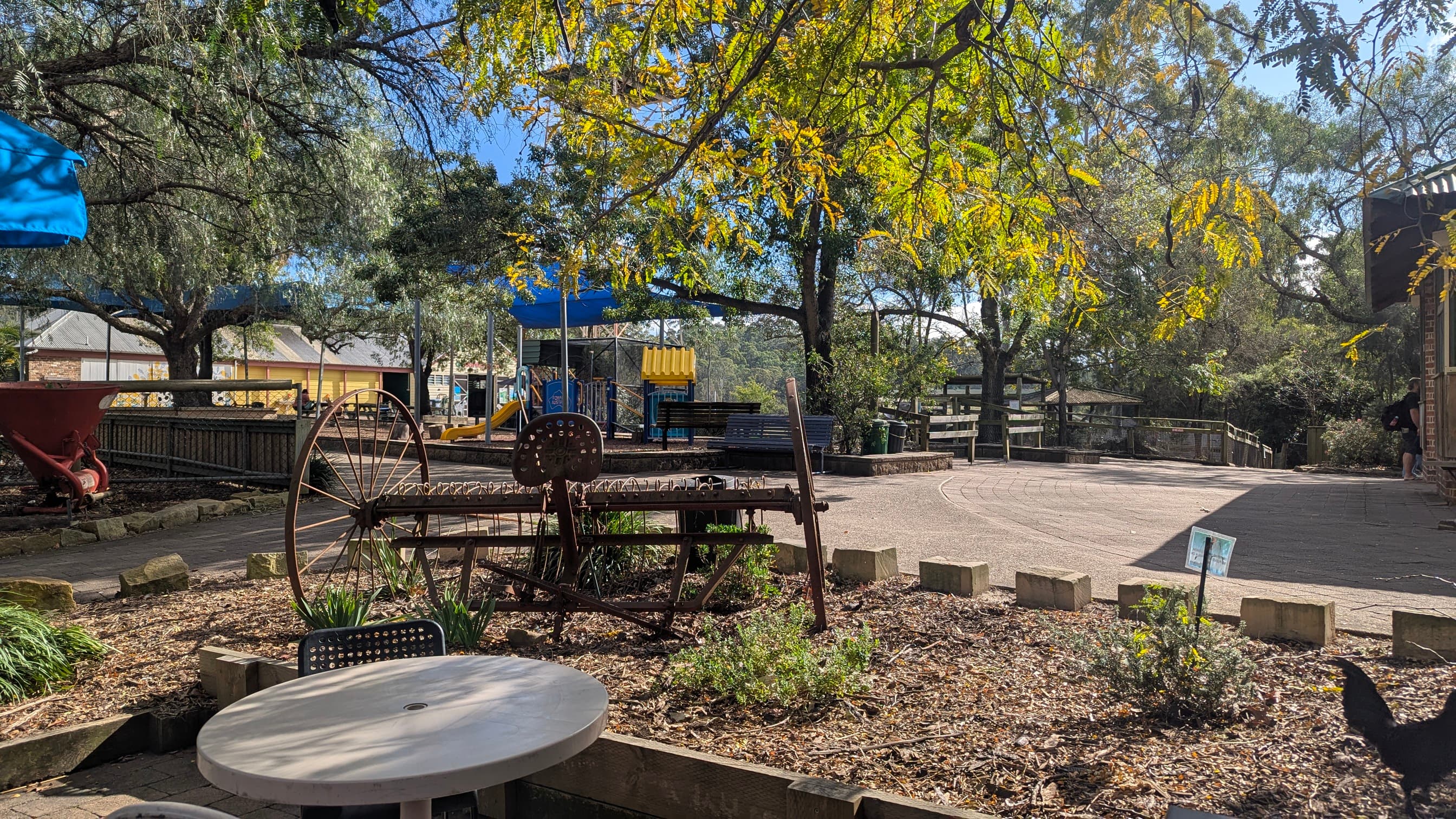 View from a cafe outdoor seating area towards a playground with old farm equipment in the foreground.