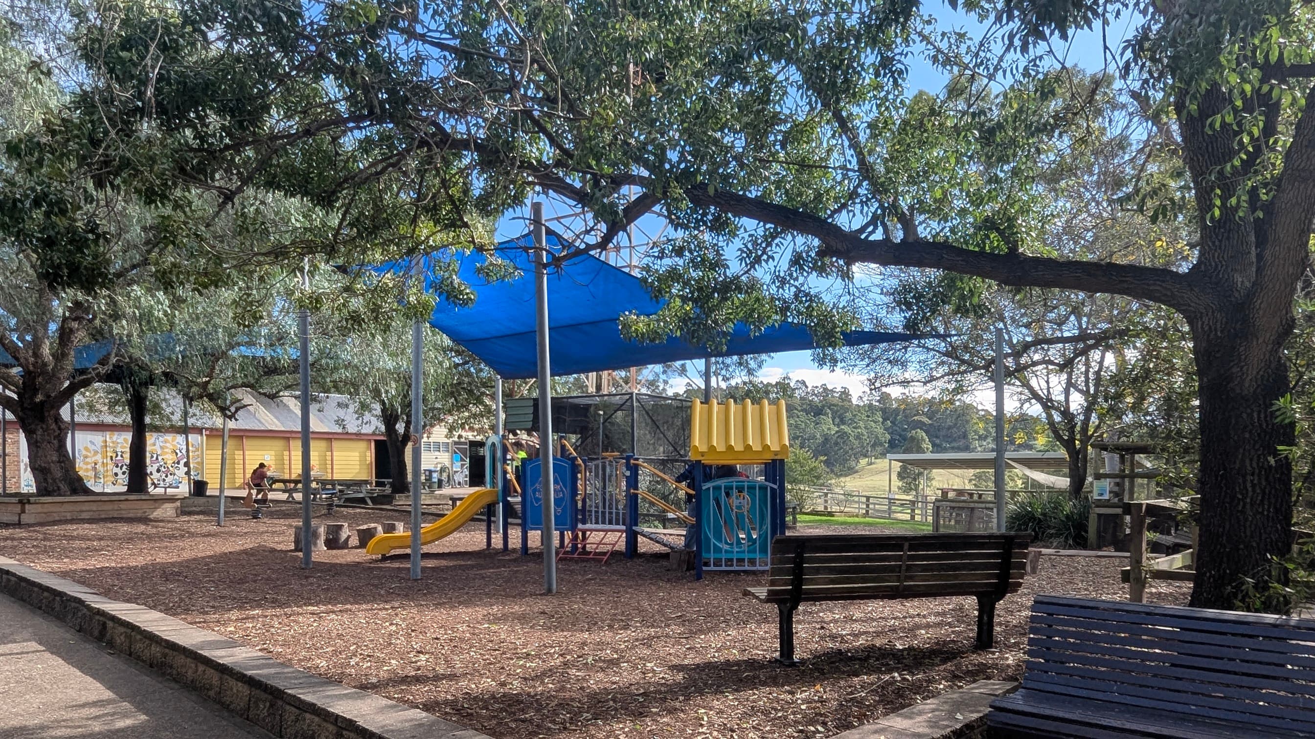 Children's playground with a slide and climbing structures under a blue shade sail.