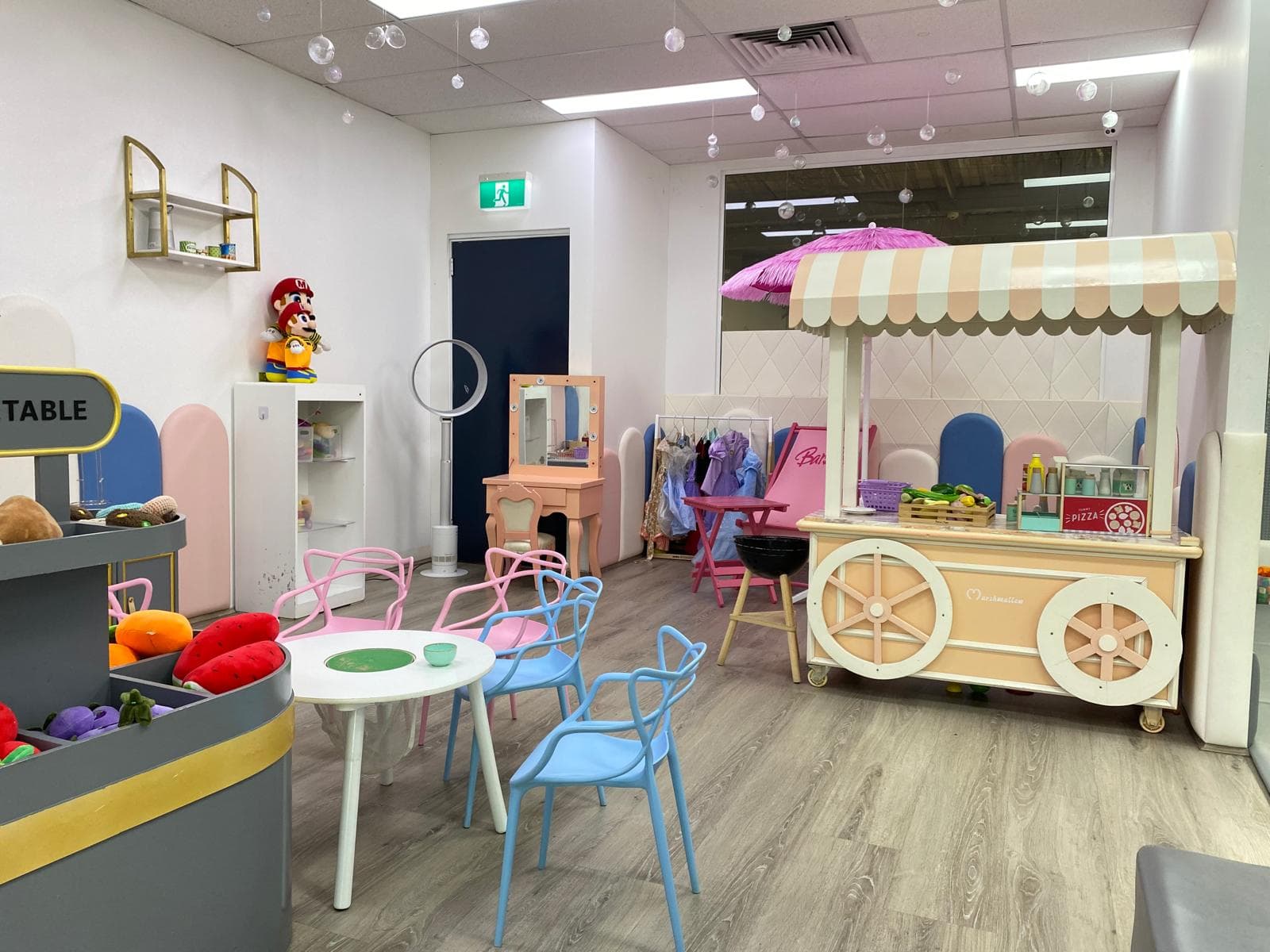 Imaginative play area with a pink striped food cart, a dressing table, and small tables and chairs.