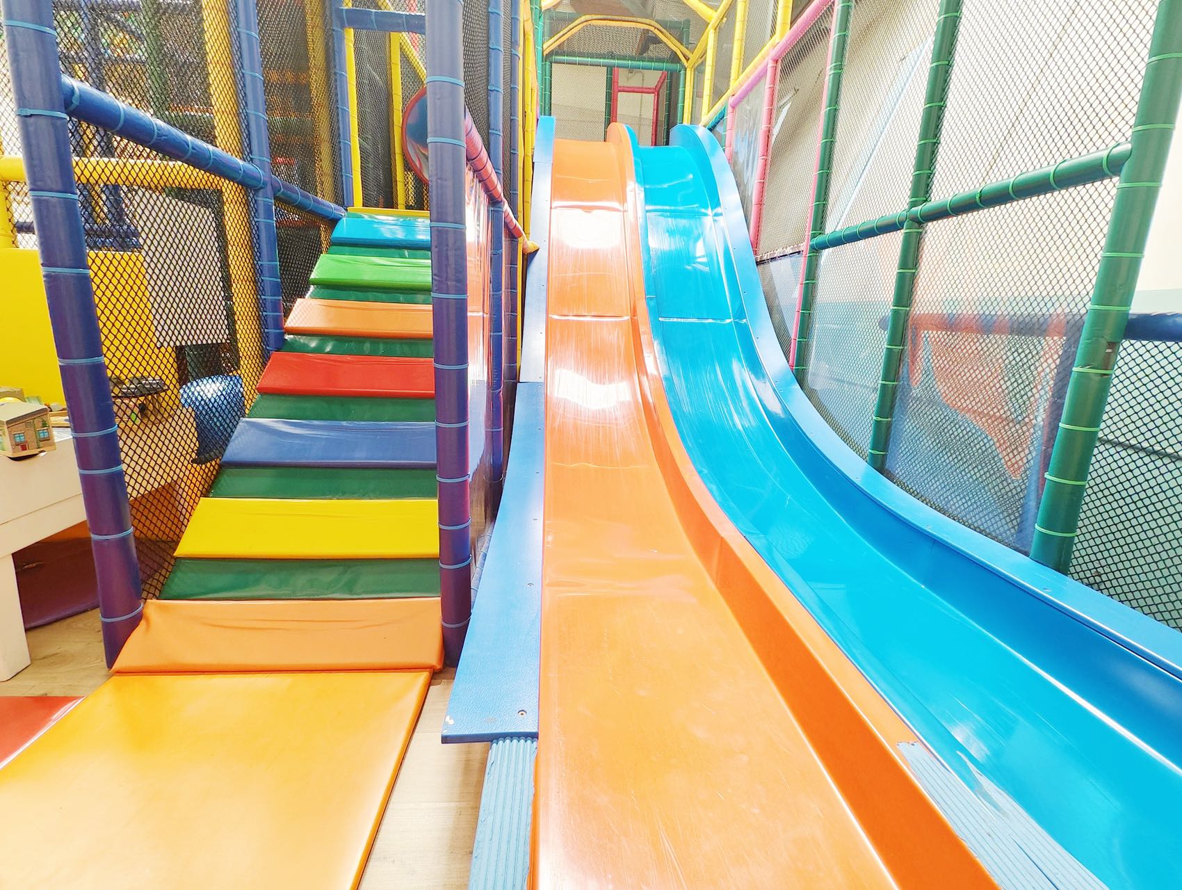 A large indoor playground with a colorful staircase and two slides, one orange and one blue.