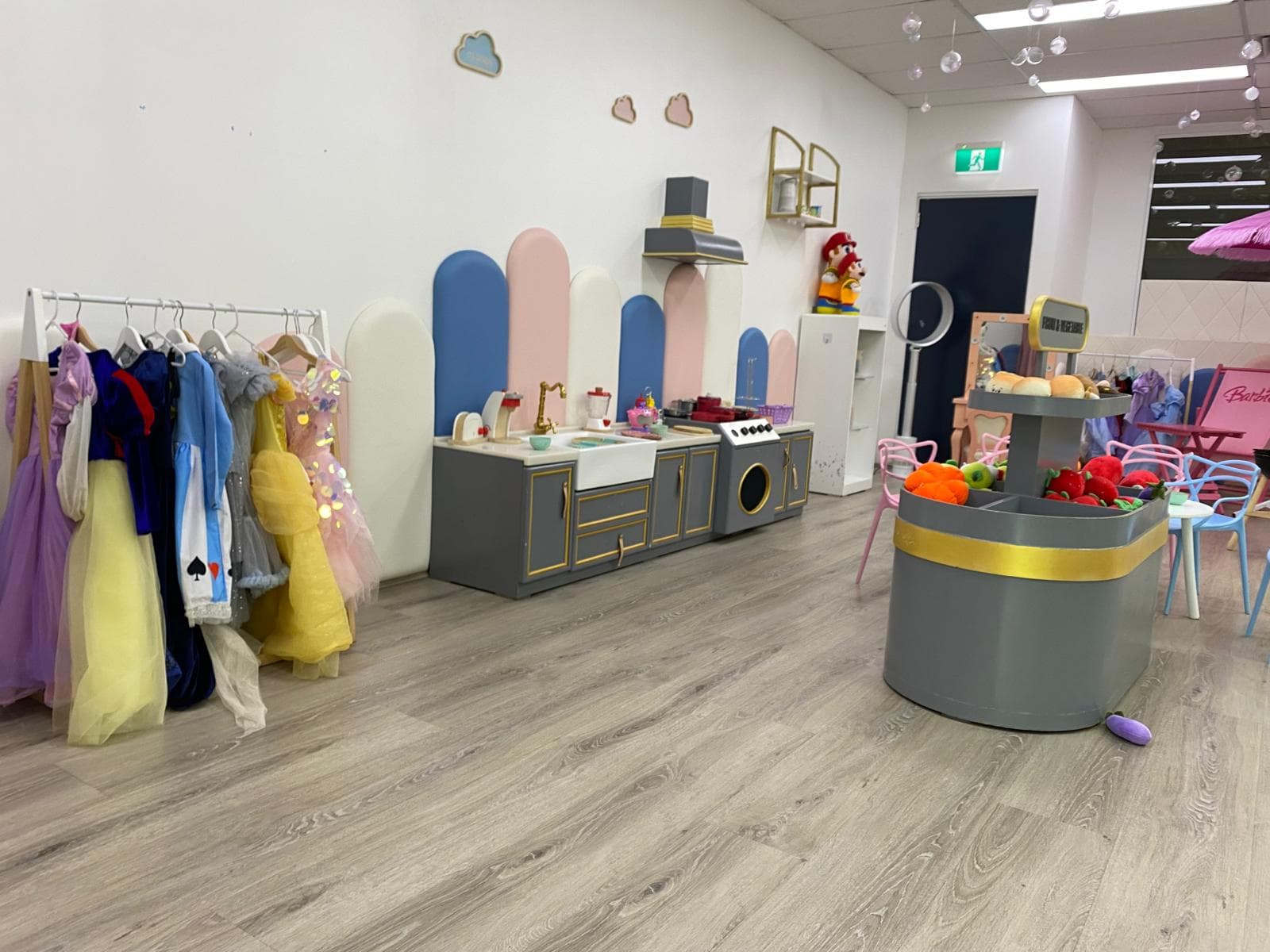 Imaginative play area with a dress-up rack, a play kitchen, and a market stall with toy vegetables.