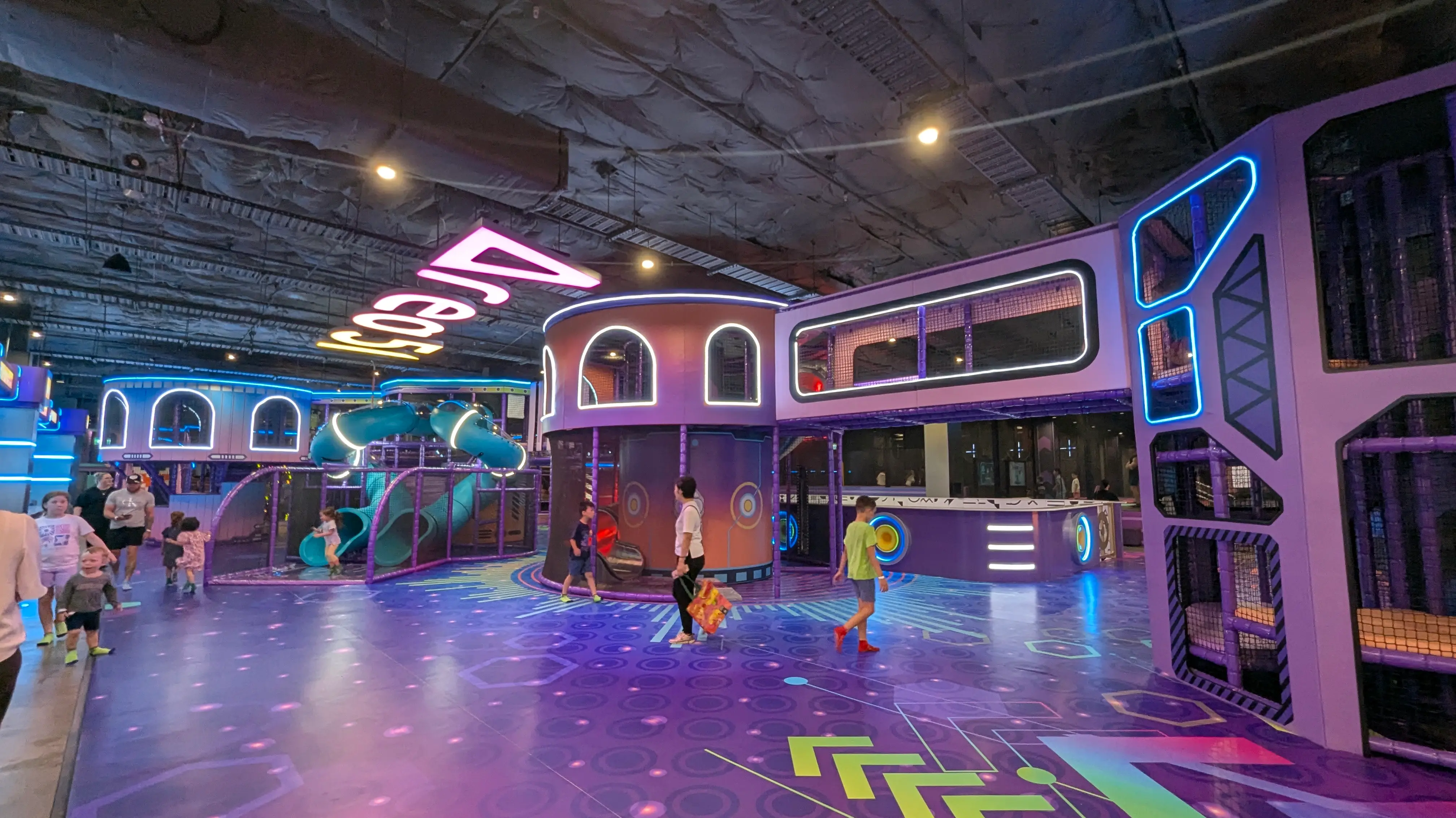 Large alien-themed play zone with a teal spiral slide, climbing tubes, and a wide, open purple floor for strollers.