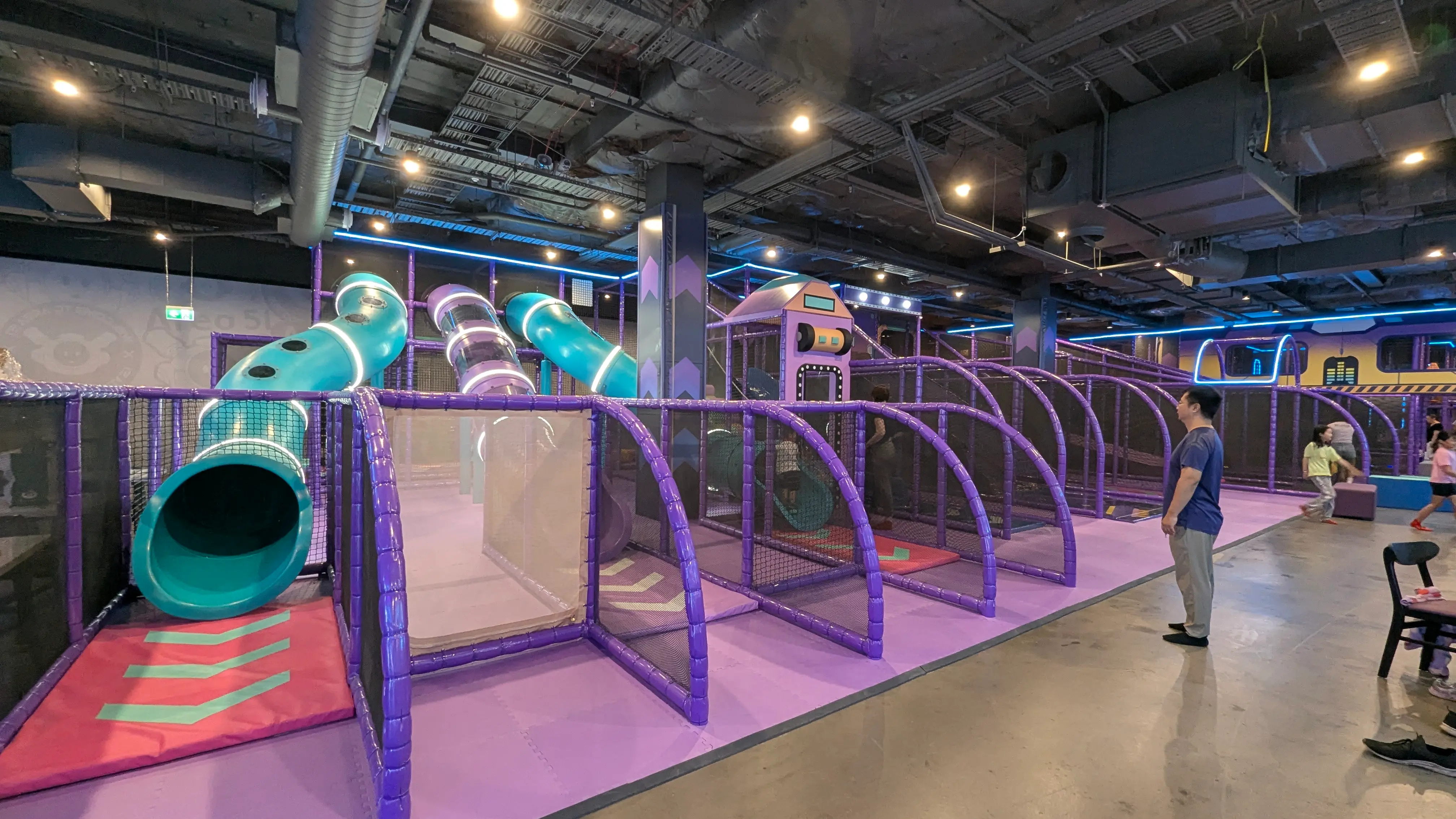 Large purple play structure featuring teal tube slides and enclosed mesh netting for safety.