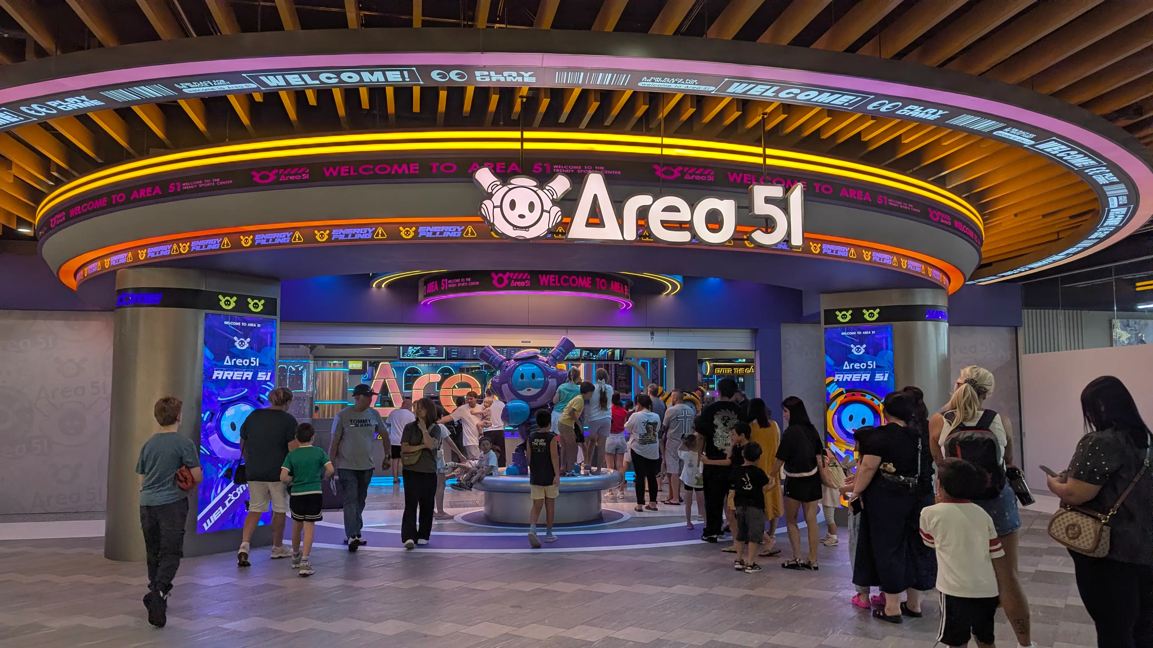 Wide, step-free entrance to Area 51 featuring bright LED signs and a large, flat paved entryway for strollers.
