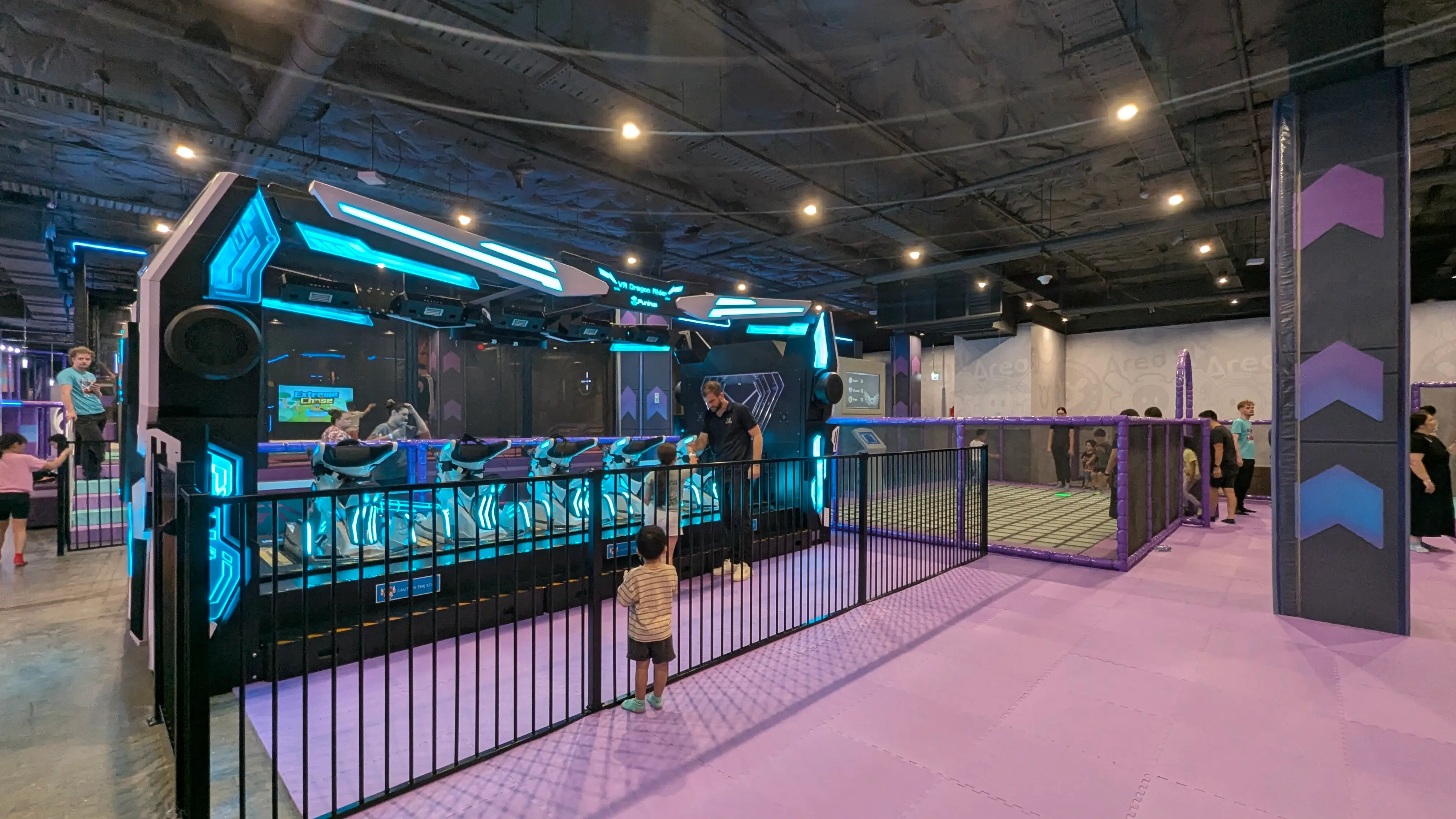 Futuristic VR motion ride with glowing blue lights, fenced for safety, on a flat purple padded floor.