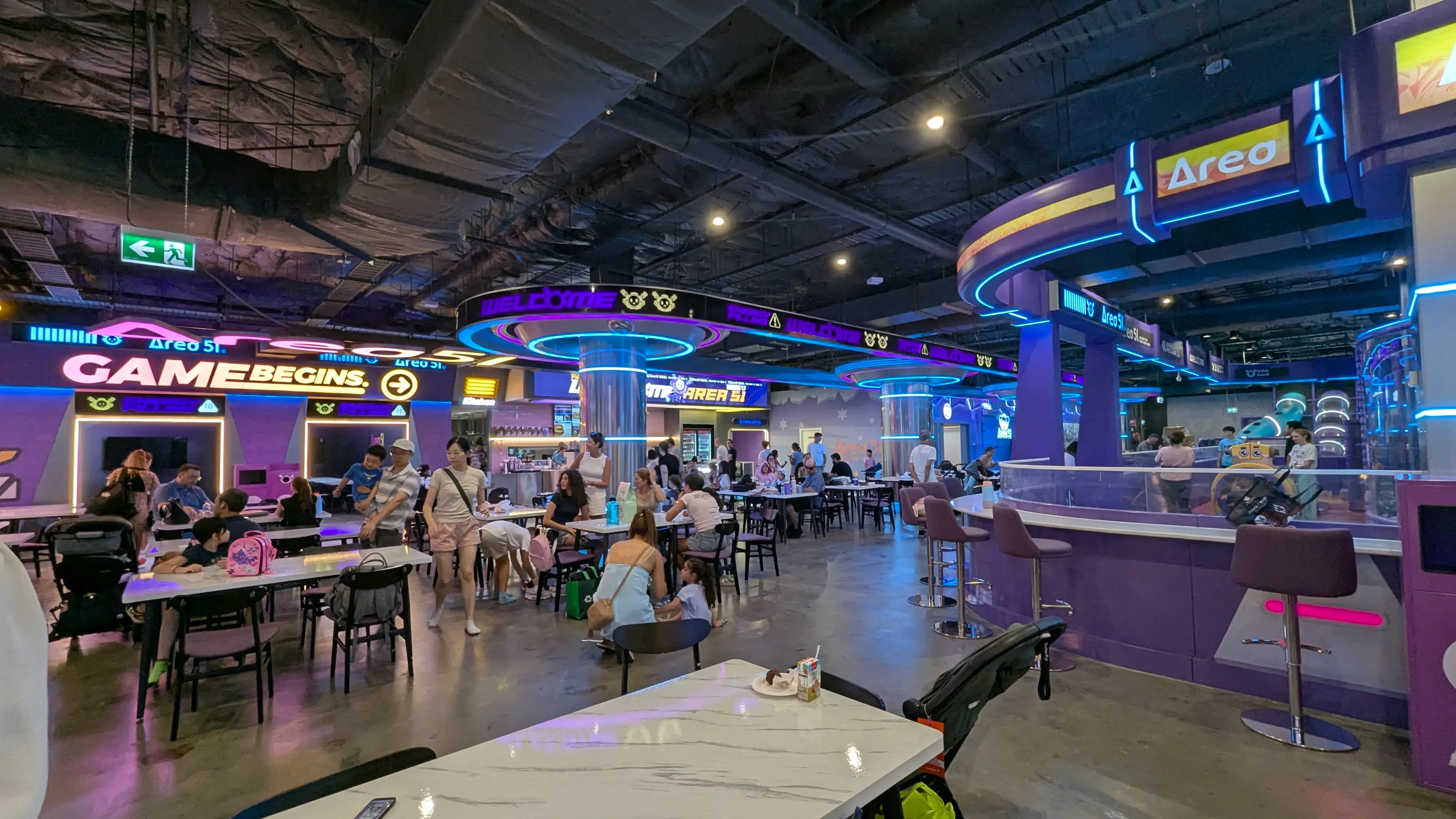 Spacious indoor cafe with ample table seating, high-top chairs, and a purple sci-fi theme near the play areas.