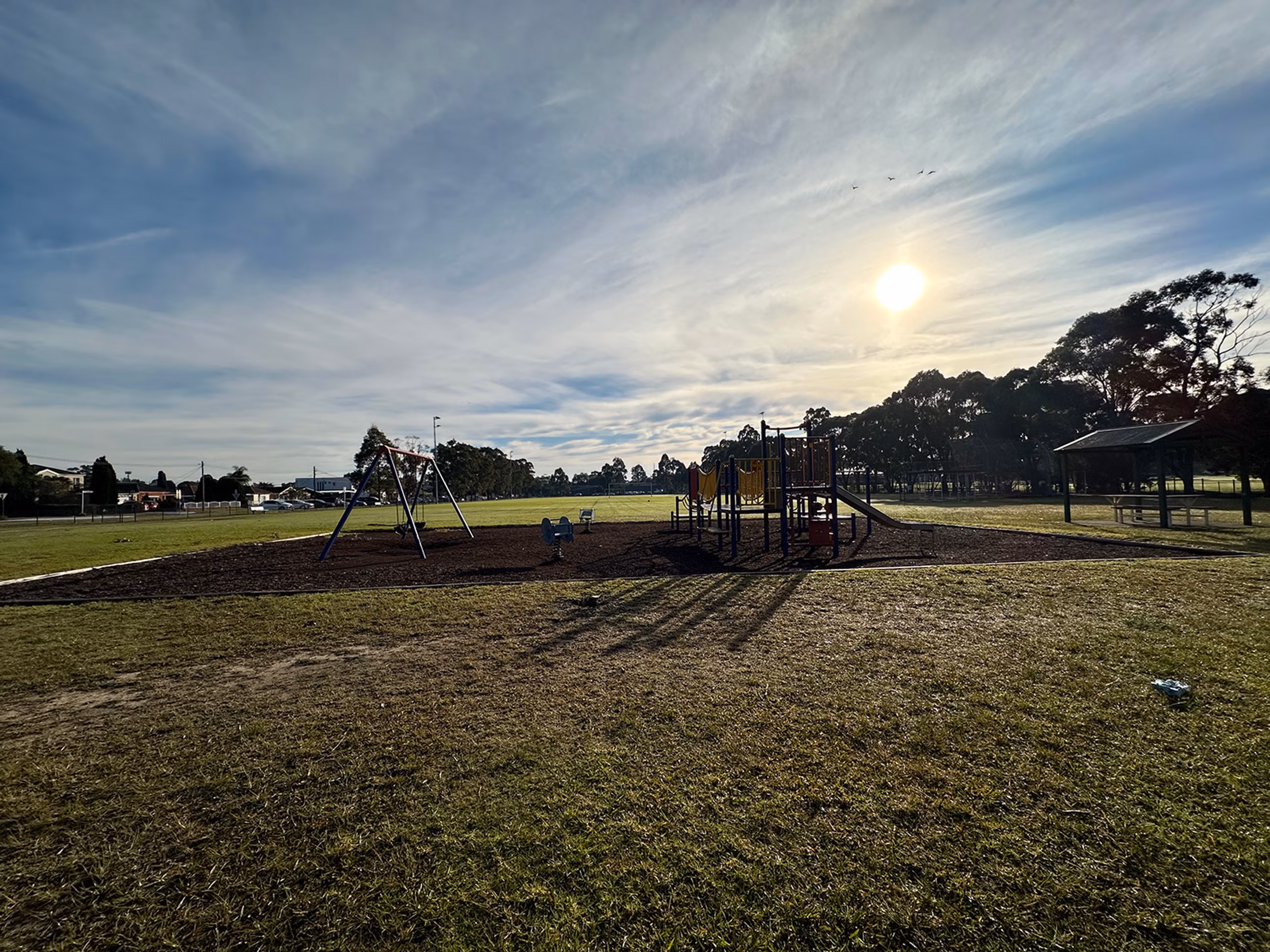 A children's playground with swings, a climbing frame and a slide on a bright day.