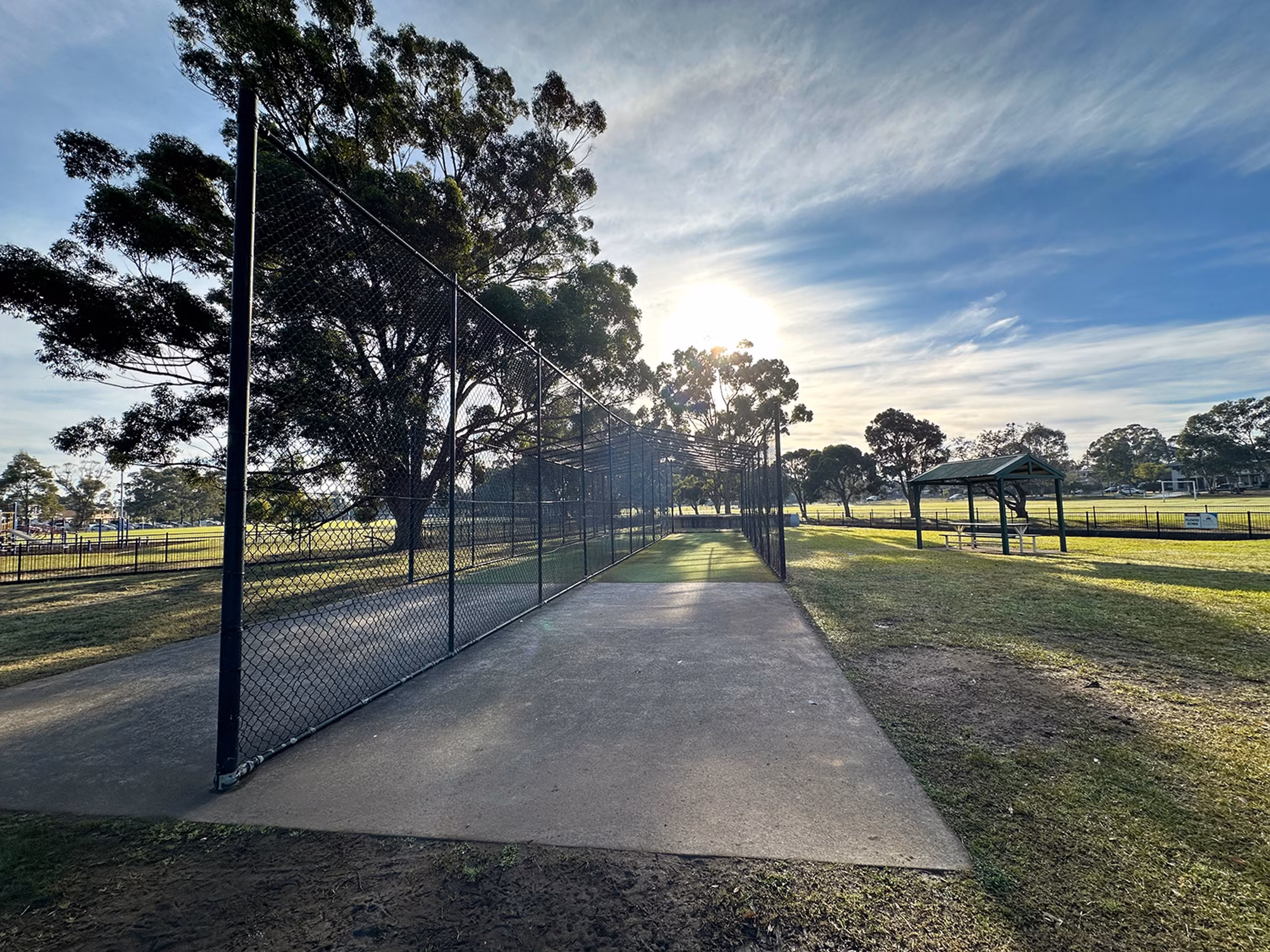 Outdoor, enclosed cricket nets on a concrete slab at the park.