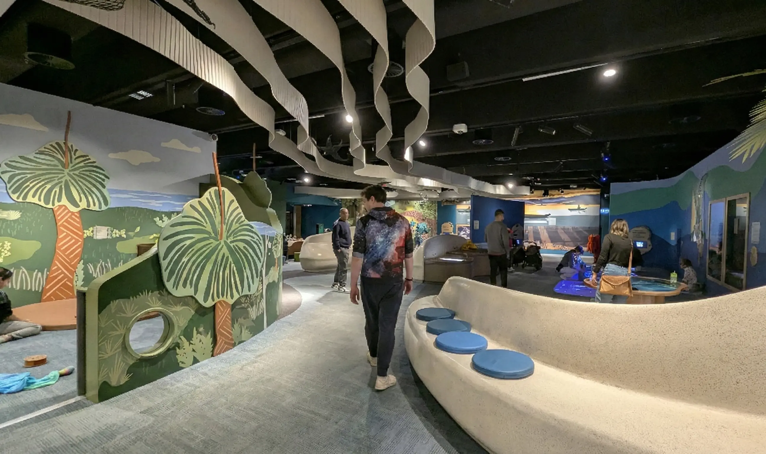 Spacious indoor learning area with wavy ceiling banners, curved benches, and colorful wall graphics for kids.