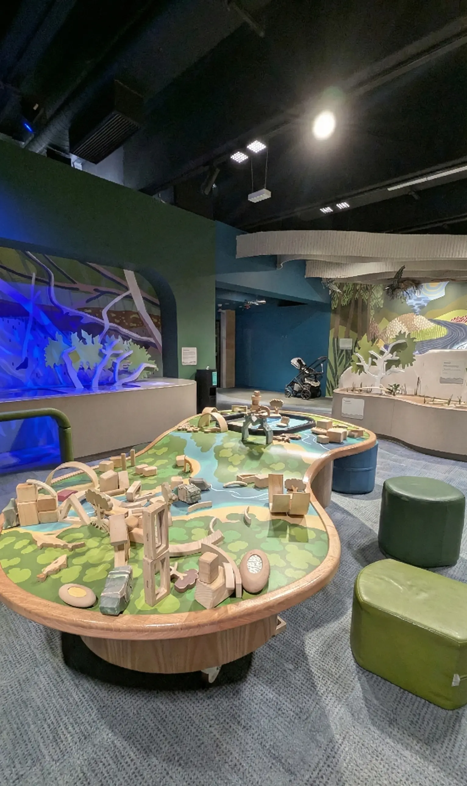 Child-sized play table with wooden blocks shaped like a landscape, located in an immersive learning gallery.