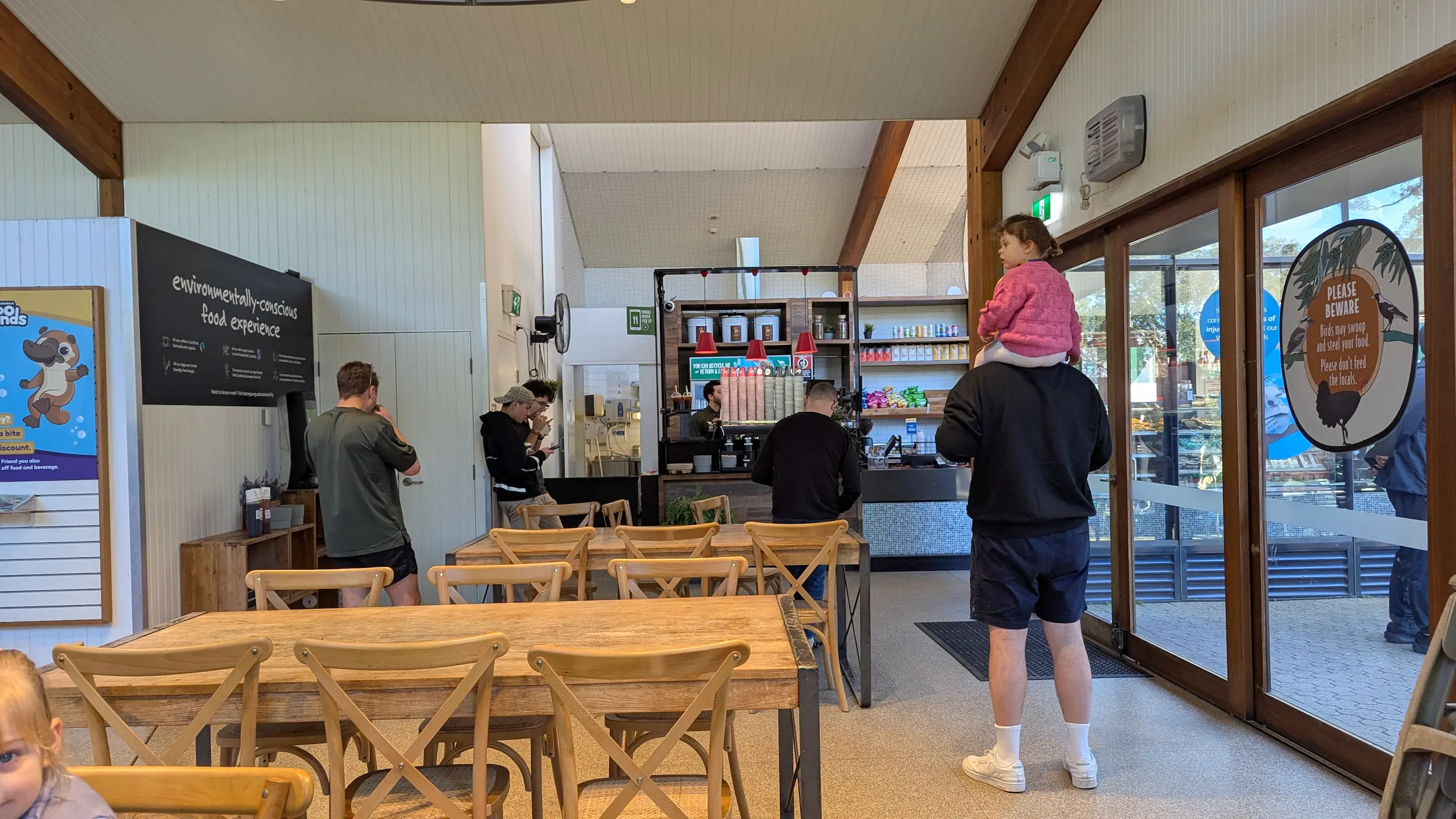 A spacious, indoor cafe with wooden tables, high ceilings, and a clear "environmentally-conscious" sign.