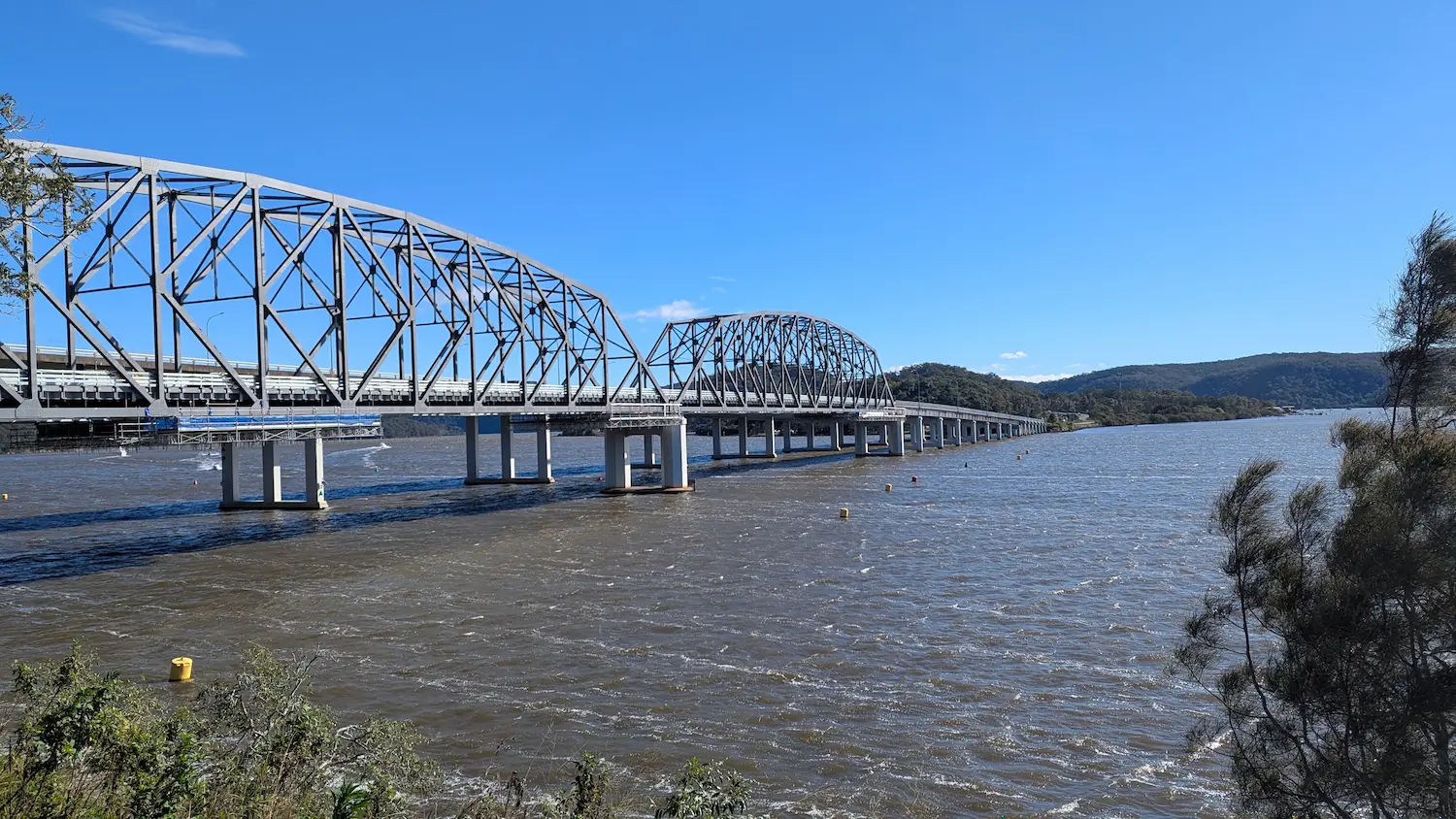 View of the Hawkesbury River Bridge, a large steel truss structure crossing the water, seen from the paved Kangaroo Point lookout.