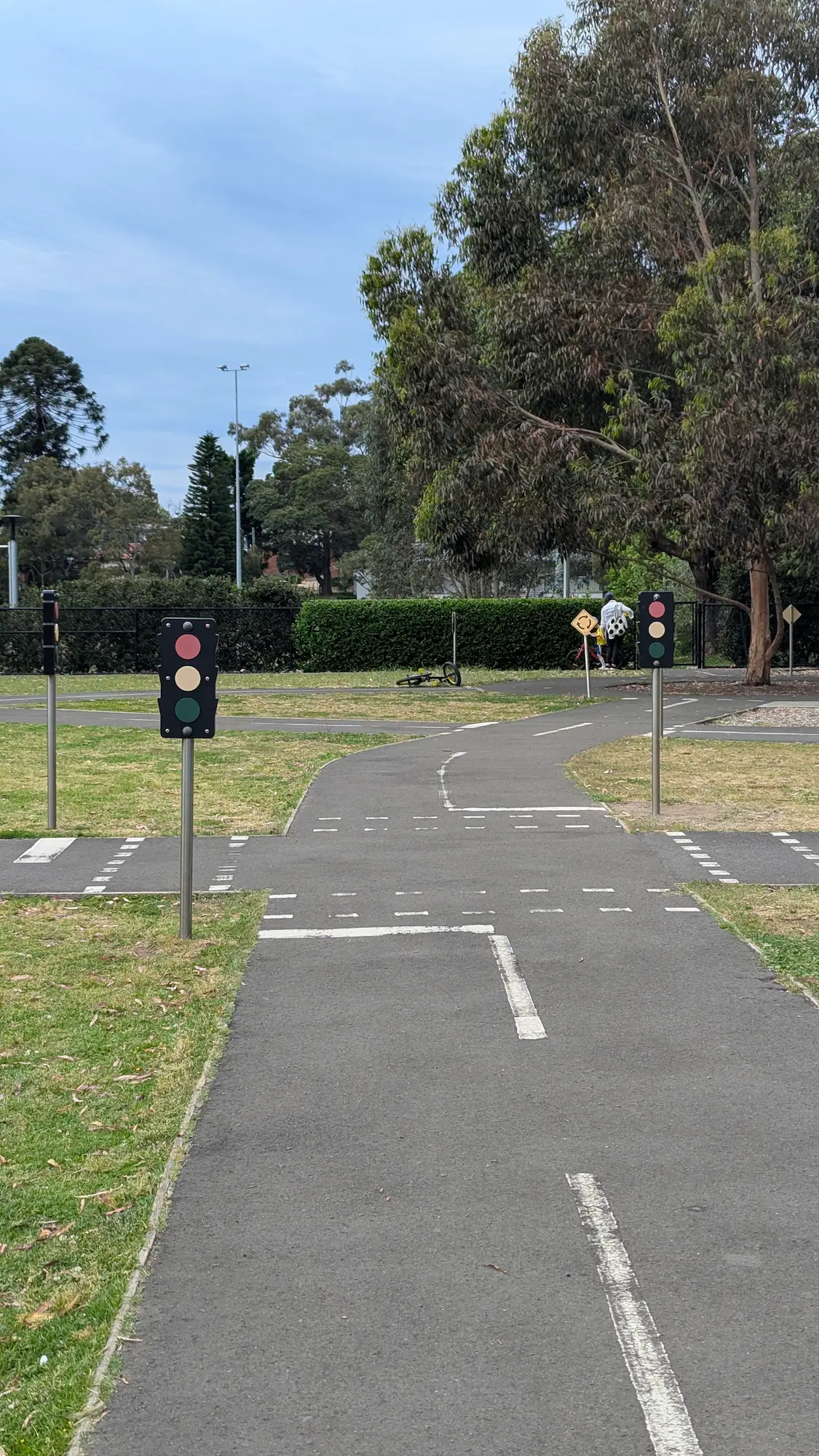 A miniature road intersection on a scooter track featuring white lane markings and play traffic lights.