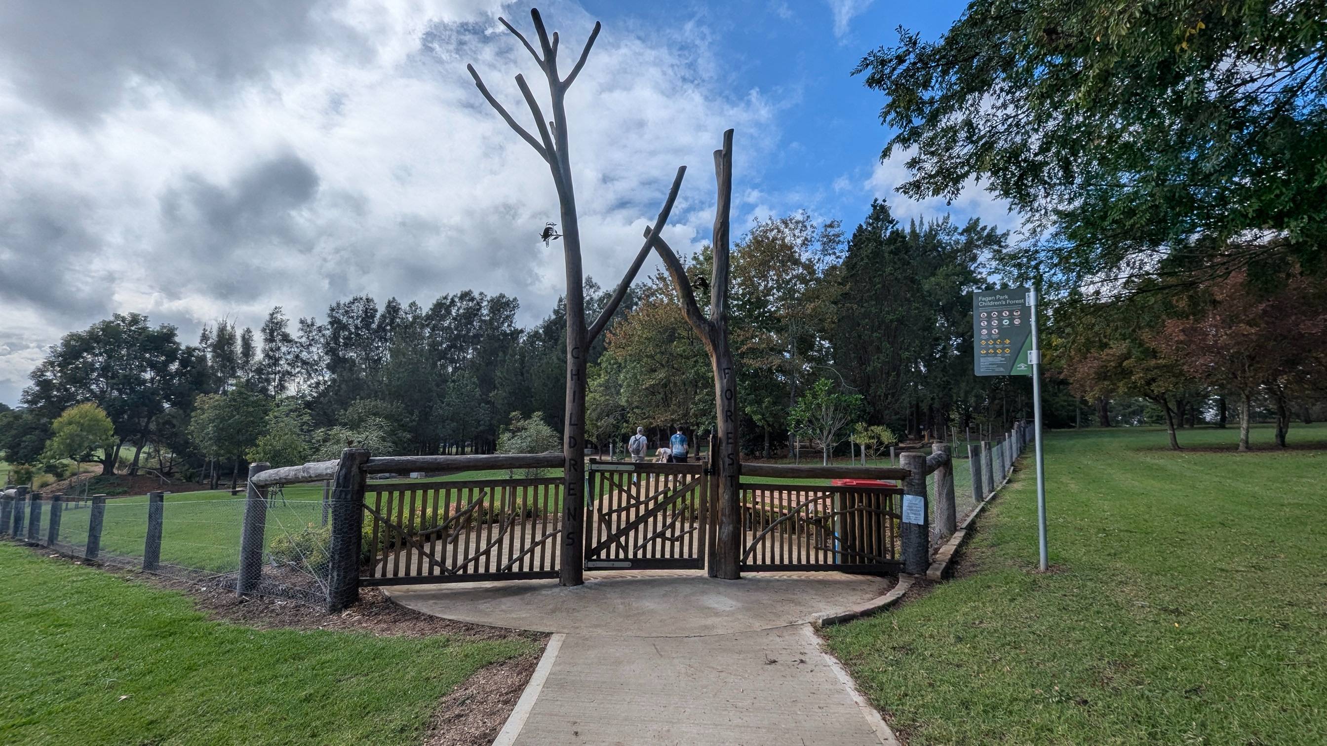 Wooden fence with two trees either side of the entry gate to the playground.