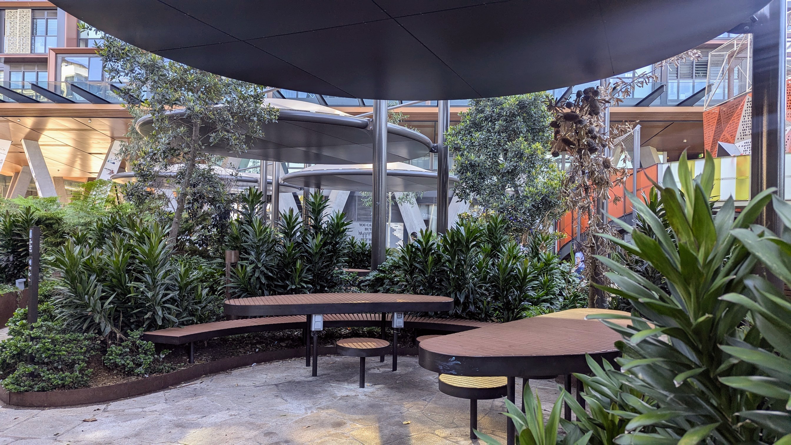Modern wooden picnic tables surrounded by greenery under a shelter.