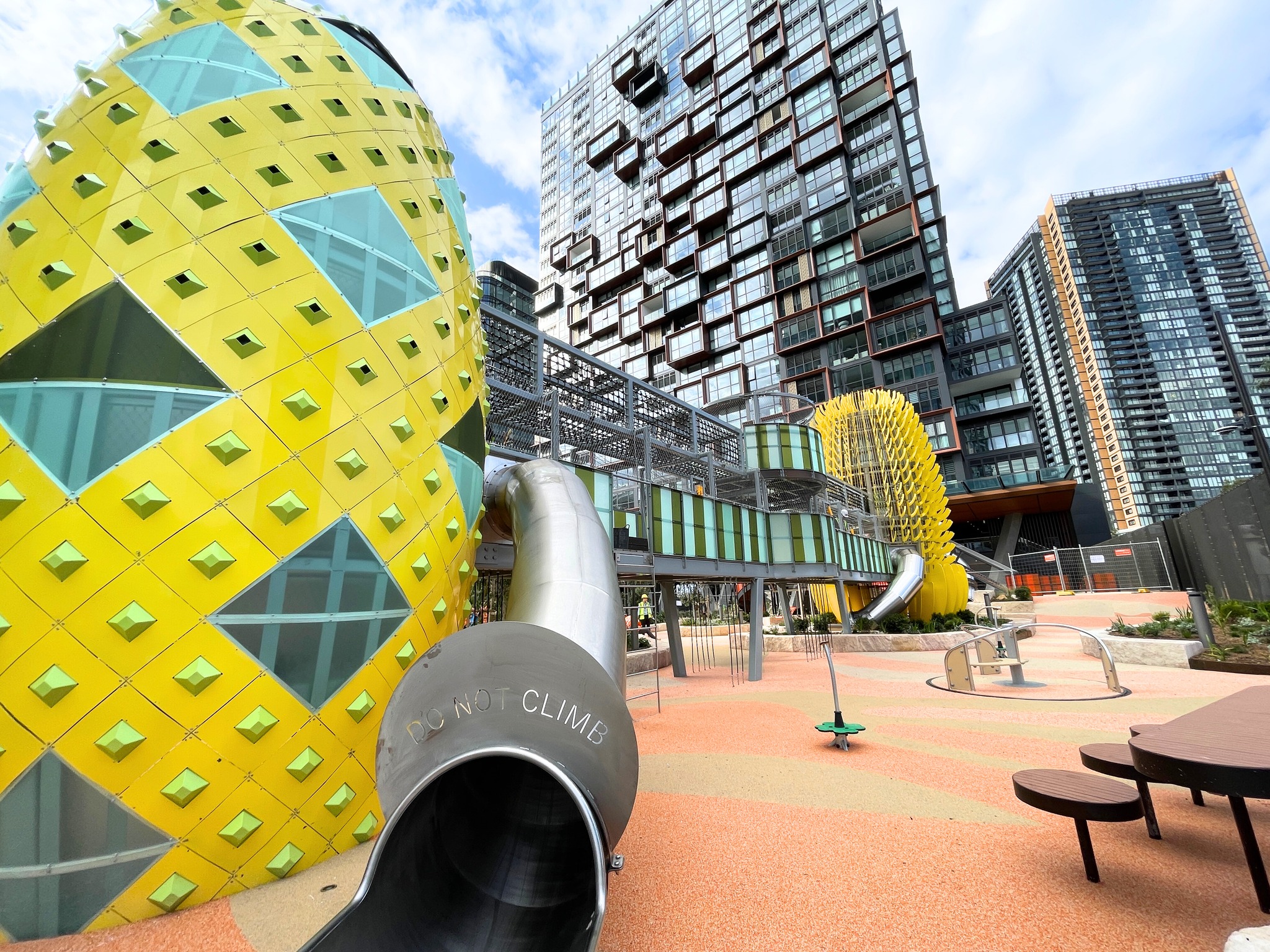 Bright yellow playground tower with slide and a bridge to another tower.