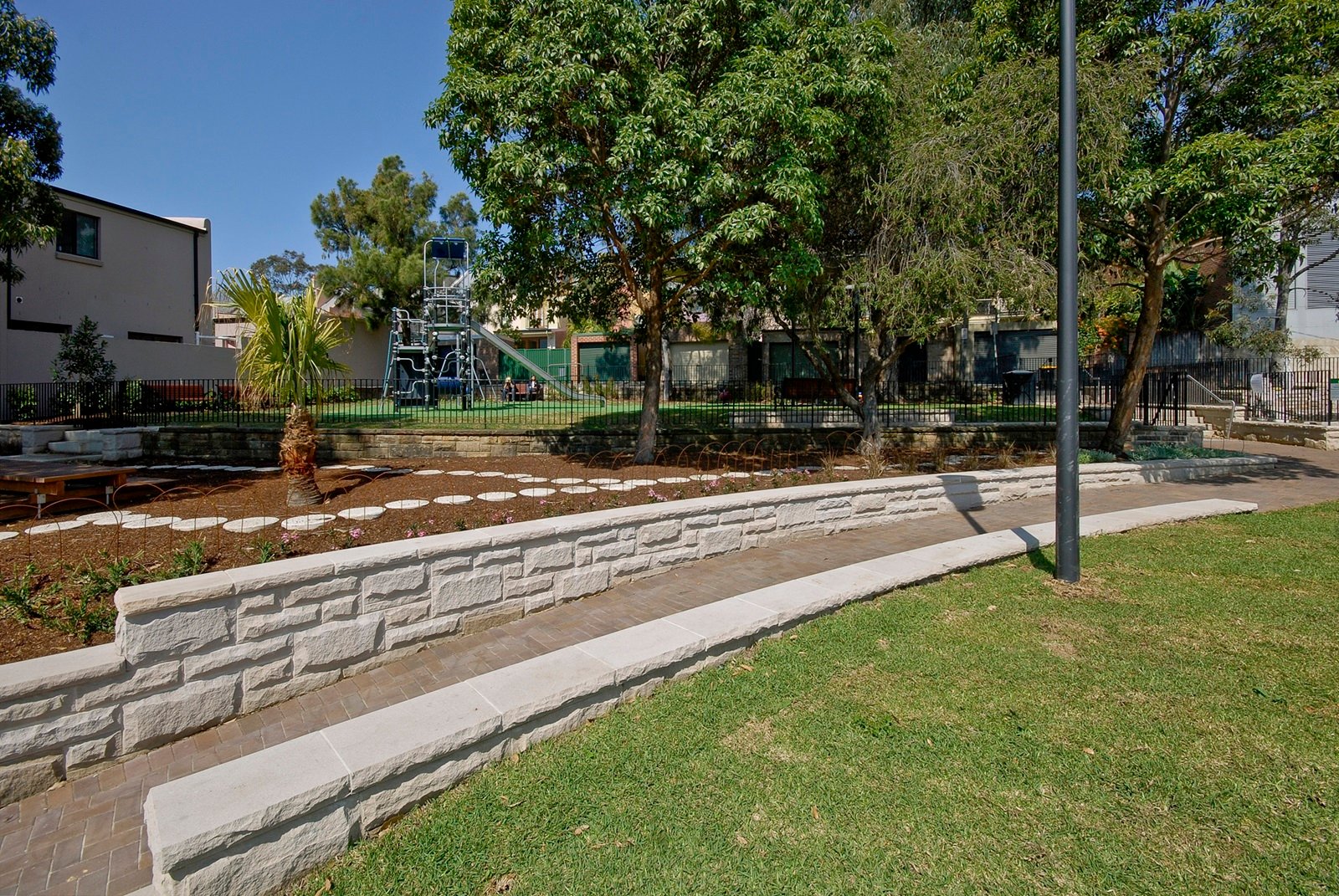 Stone wall and paved pathway leading to the playground at Charles Kernan Reserve.