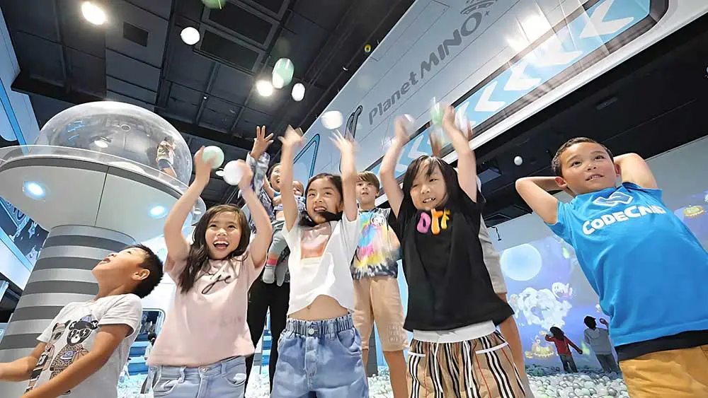 Children with raised arms celebrating in an interactive indoor play space with bubble machines and modern exhibits at Planet Mino Warringah Mall