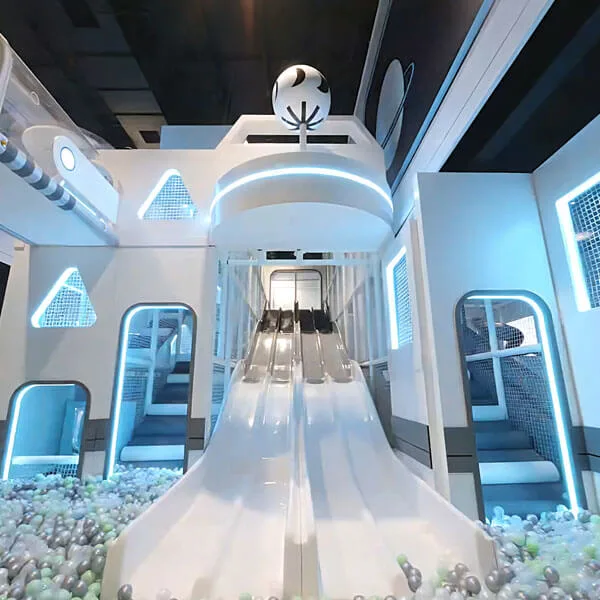 Modern white indoor playground with curved slide, climbing structures, and futuristic spaceship-themed design with blue LED lighting and safety netting.