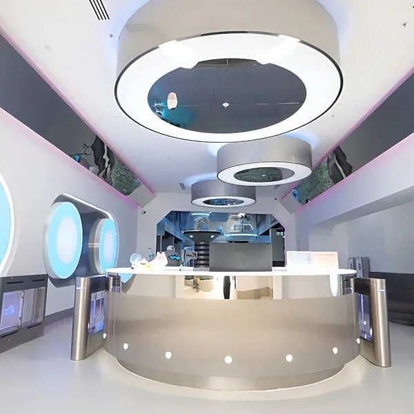 Futuristic indoor play center with white curved architecture, circular ceiling features, central reception desk with turnstile entry, and colorful lighting throughout multi-level space.