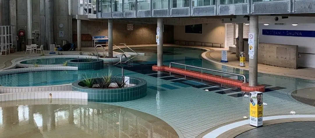 Indoor aquatic center with multi-level pools, including shallow wading areas and a circular planter feature, plus accessible ramps and safety railings throughout.