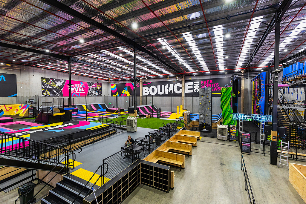 Wide view of the BOUNCE Cromer arena showing the interconnected trampoline floor, climbing wall and BOUNCE branding under an industrial roof.