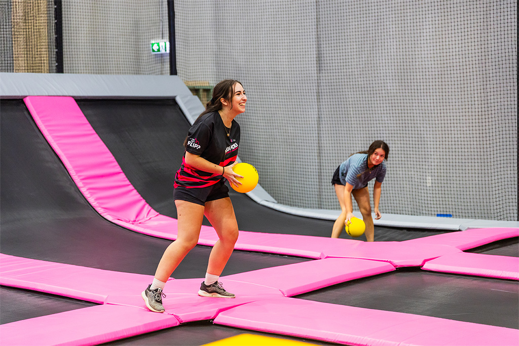 Two players holding yellow dodgeballs on the pink-padded interconnected trampolines at BOUNCE Cromer.
