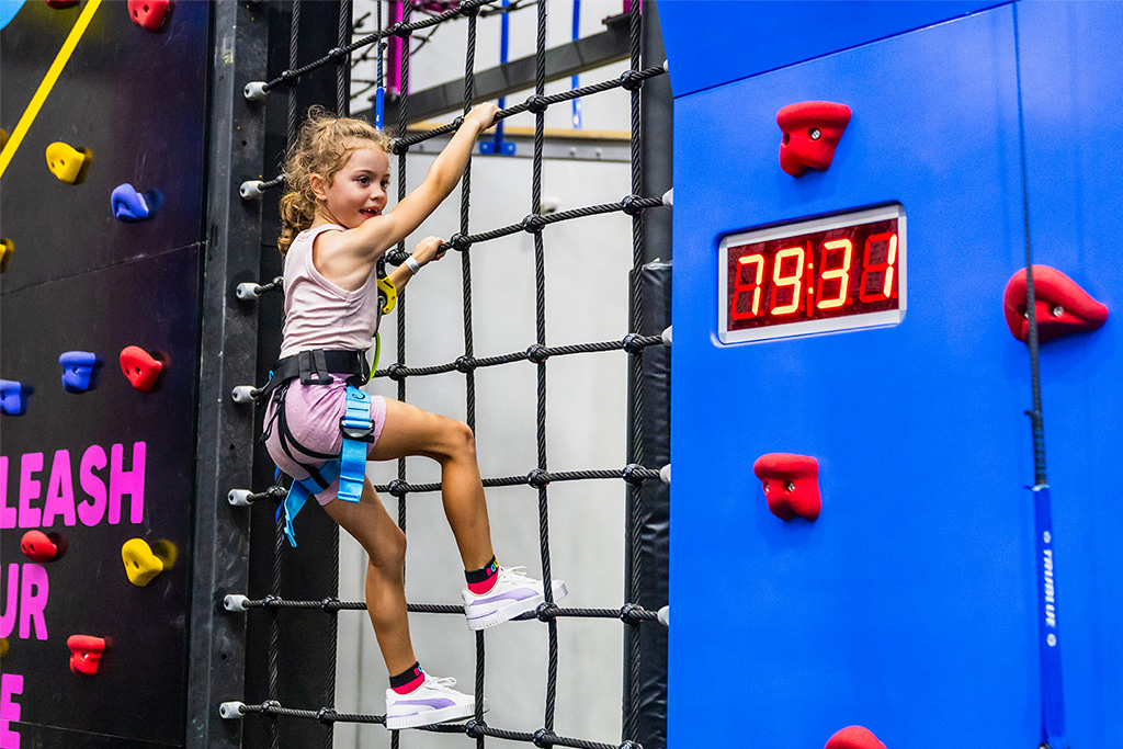 A harnessed child climbing a coloured holds-and-net climbing wall at BOUNCE Cromer.