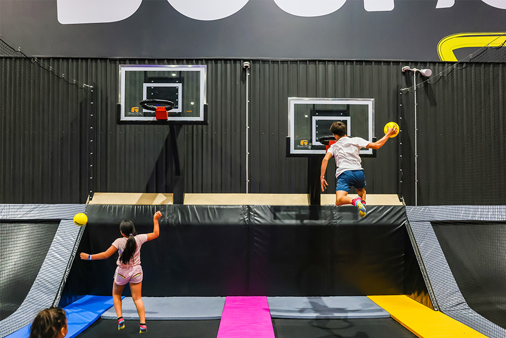 Children jumping on trampolines and dunking balls into basketball hoops in the indoor arena at BOUNCE Homebush.