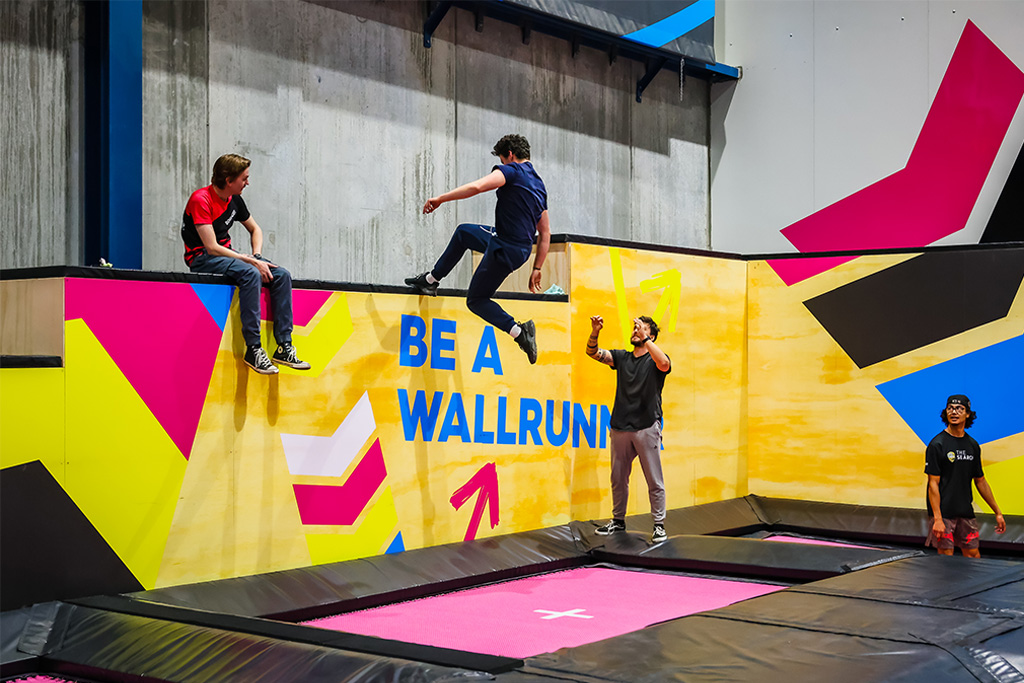 Kids using trampolines to run up a painted wall in the Wall Climb zone at BOUNCE Homebush.