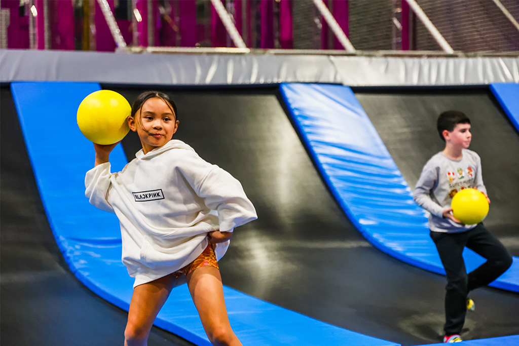 Two children playing dodgeball with yellow balls on angled trampolines at BOUNCE Homebush.