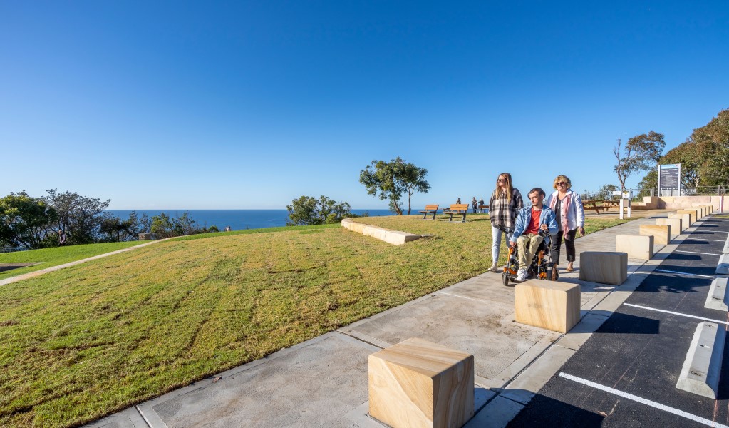 Visitors including a wheelchair user on the accessible concrete path beside the carpark at Crackneck Point Lookout