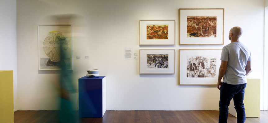 A visitor viewing framed artworks and a ceramic piece in a light-filled exhibition space at Manly Art Gallery & Museum.