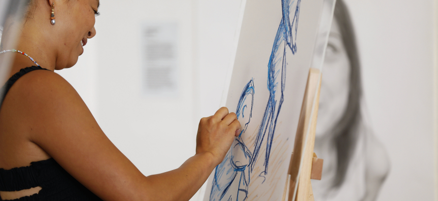 A person sketching a figure in blue pastel on an easel during an art activity at Manly Art Gallery & Museum.