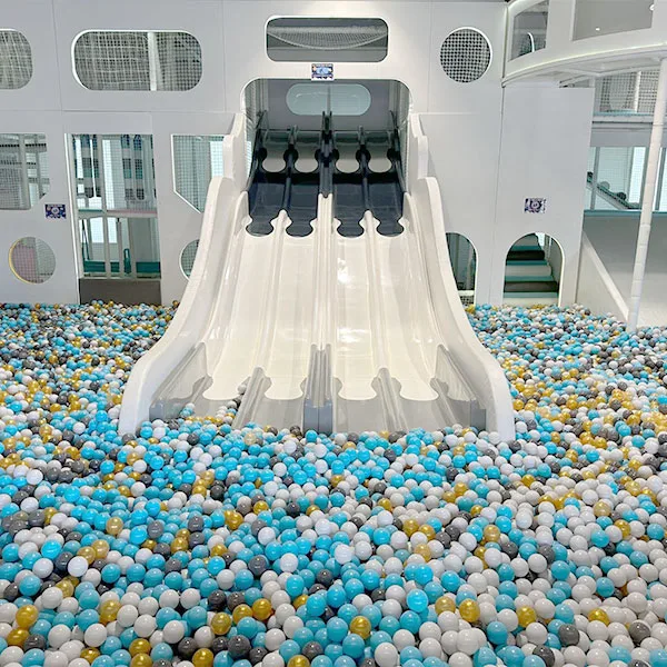 Large white slide leading into colorful ball pit with blue, white, and yellow balls at indoor play center with multi-level climbing structure