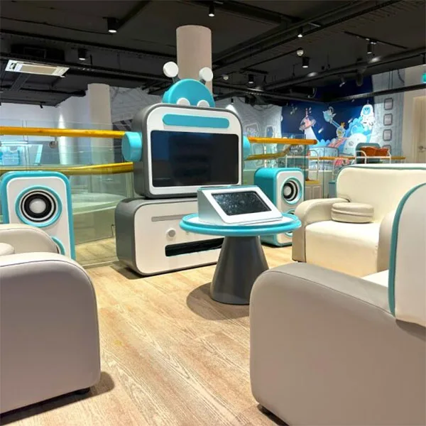 Modern interactive play area with futuristic white and teal seating pods, digital screens, and sleek robot-themed design elements in an indoor children's entertainment space.