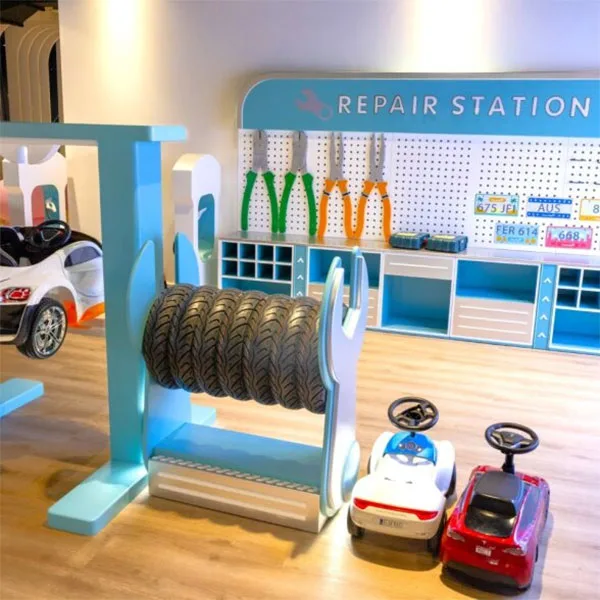 Colorful children's repair station play area with tire rack, pegboard tools, toy cars and ride-on vehicles on wooden floor