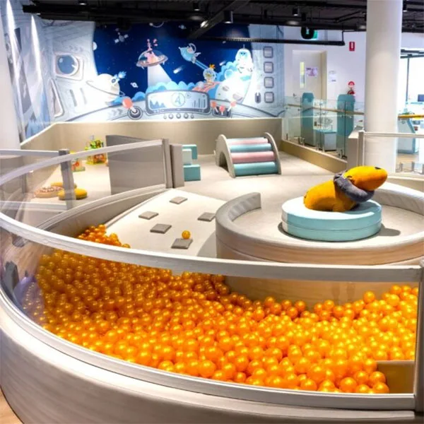 Colorful indoor play area with orange ball pit, soft play structures, and space-themed wall mural featuring cartoon characters in a spaceship setting