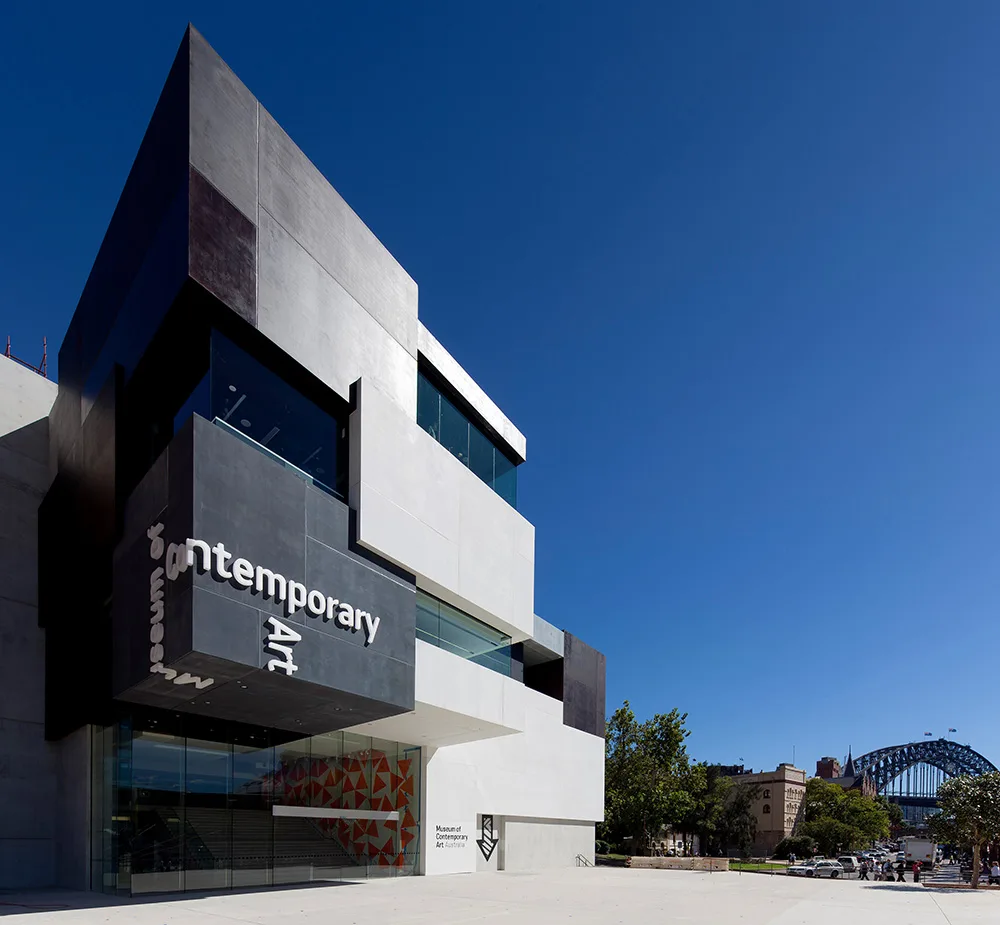 Flat, accessible paved plaza leading to the modern, glass-fronted entrance of the Museum of Contemporary Art. Harbour Bridge in background.