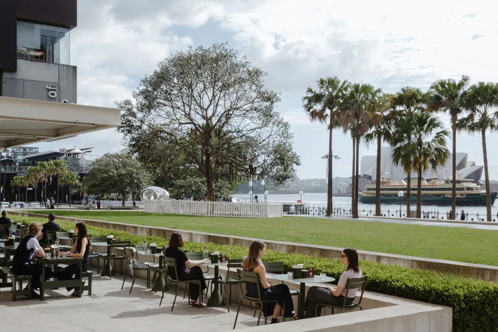 Accessible outdoor cafe patio with ample stroller space, situated right next to a safely fenced grassy lawn overlooking the Sydney Opera House.