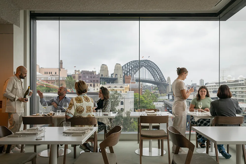Spacious, brightly lit indoor restaurant with widely spaced tables ideal for strollers, featuring floor-to-ceiling windows overlooking the harbour.