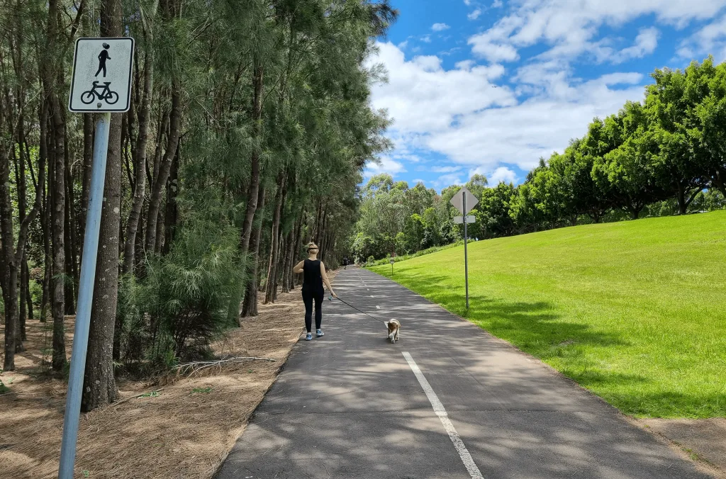 Paved shared pathway with pedestrian and cyclist symbols, lined with trees and green lawn, perfect for family walks and bike rides