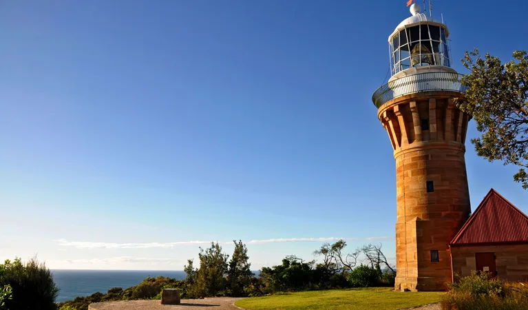 Sandstone Barrenjoey Lighthouse standing on the grassy headland above Palm Beach with the ocean behind.