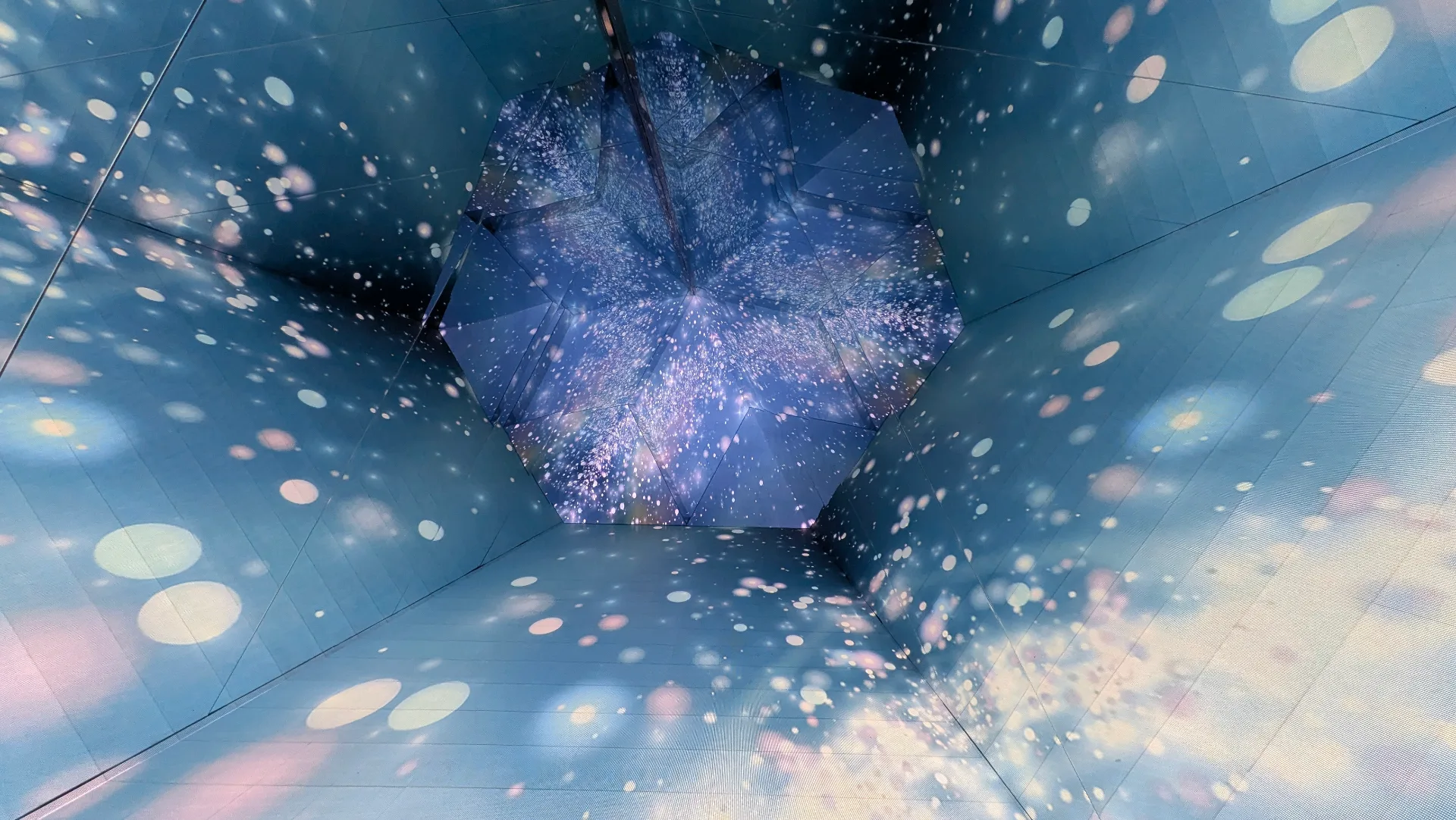 Immersive digital display ceiling showing a starry galaxy projection with floating light orbs, creating an interactive sensory experience for visitors
