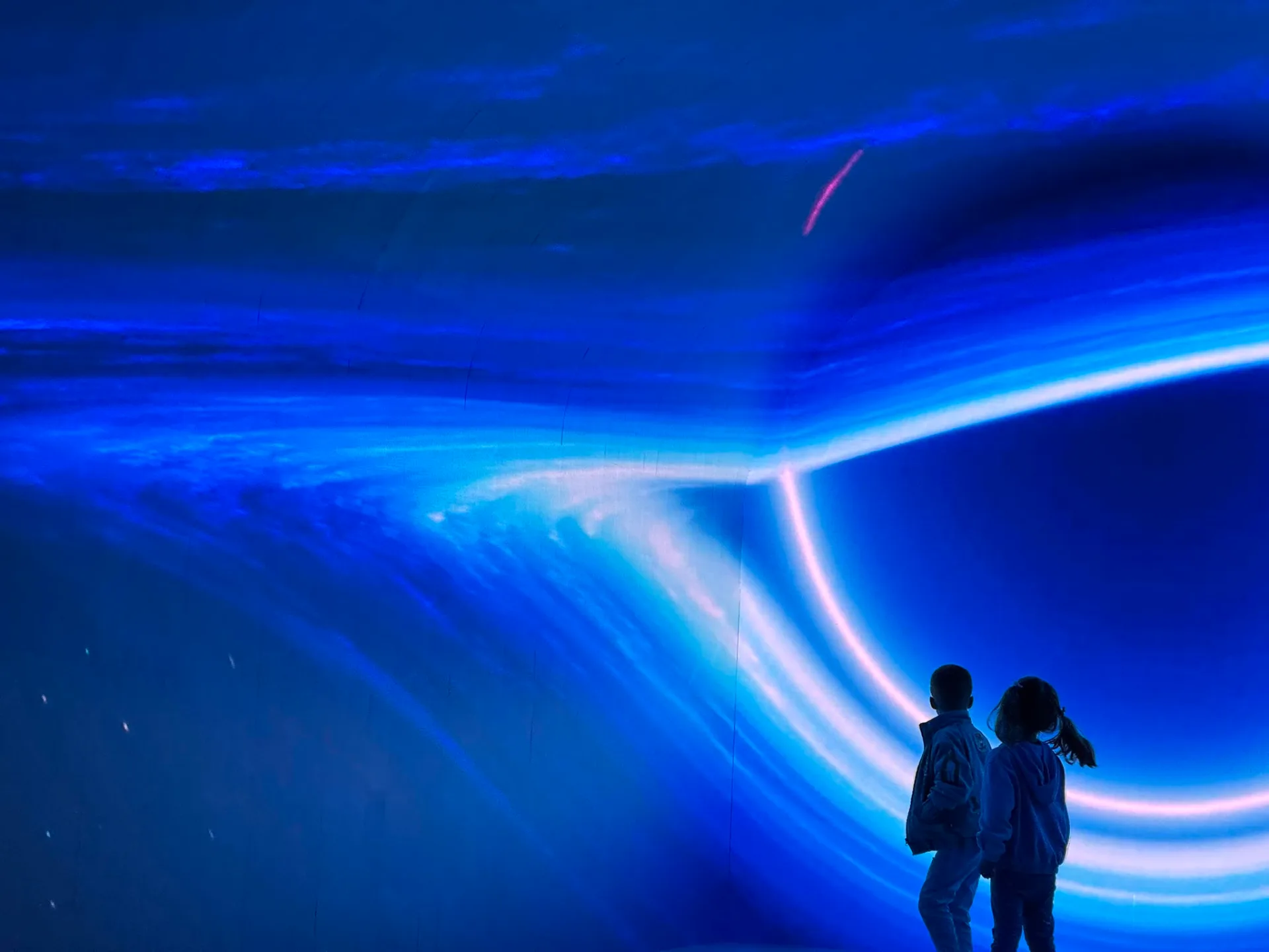 Two children silhouetted against a bright blue digital projection with streaming light beams at DigiPark Sydney's immersive interactive experience.