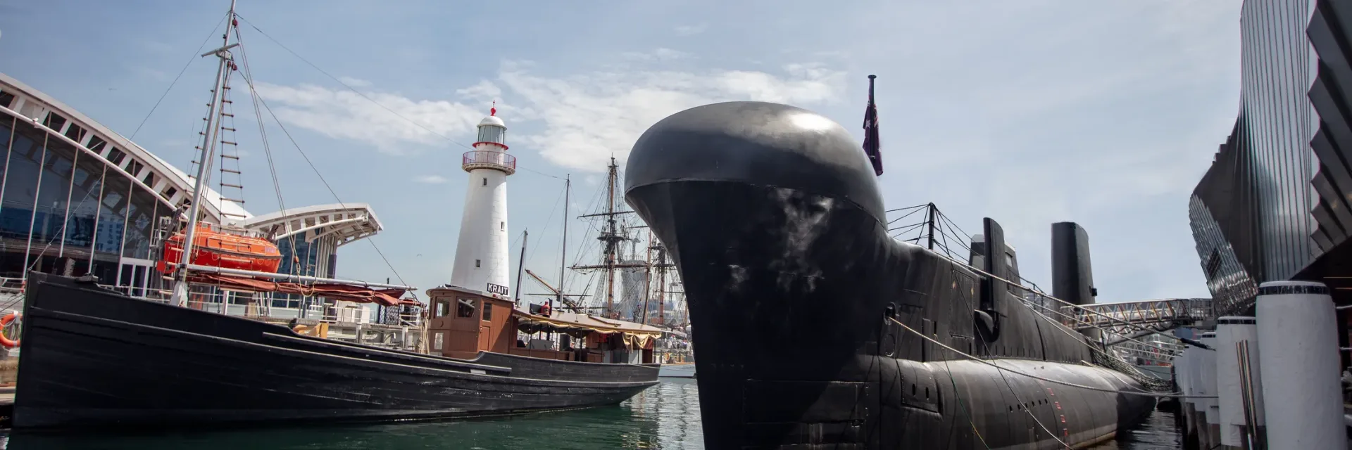 Historic naval vessels and submarine docked at waterfront museum with lighthouse, featuring interactive maritime exhibits and family-friendly exploration opportunities.