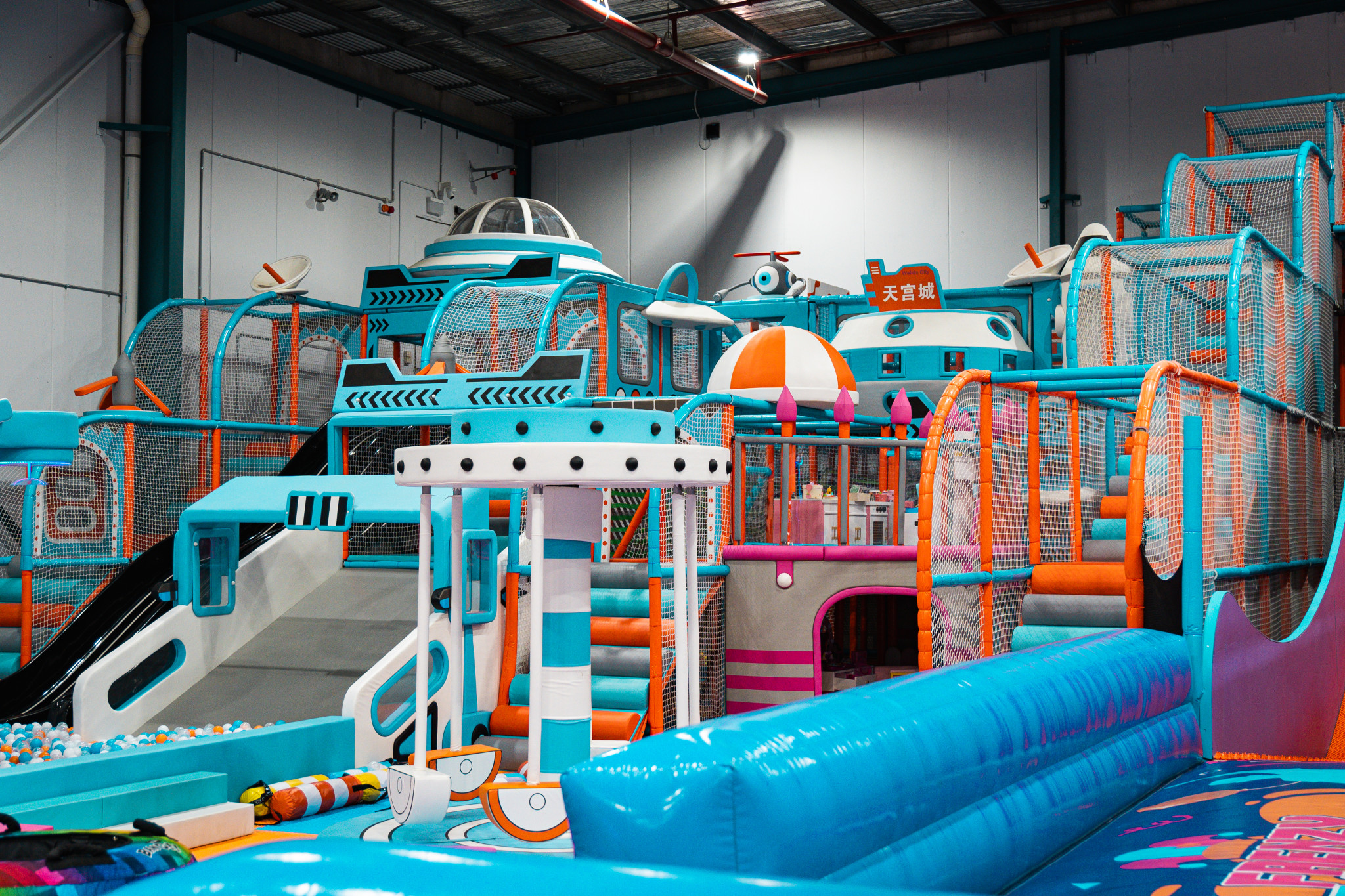 Large multi-level blue and orange soft play structure with slides, climbing frames and a ball pit in the foreground