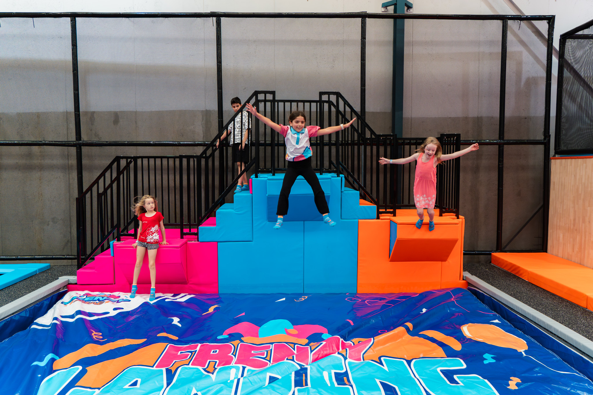 Three children jumping and posing on foam blocks above a printed Freaky Landing soft-landing airbag in the trampoline zone